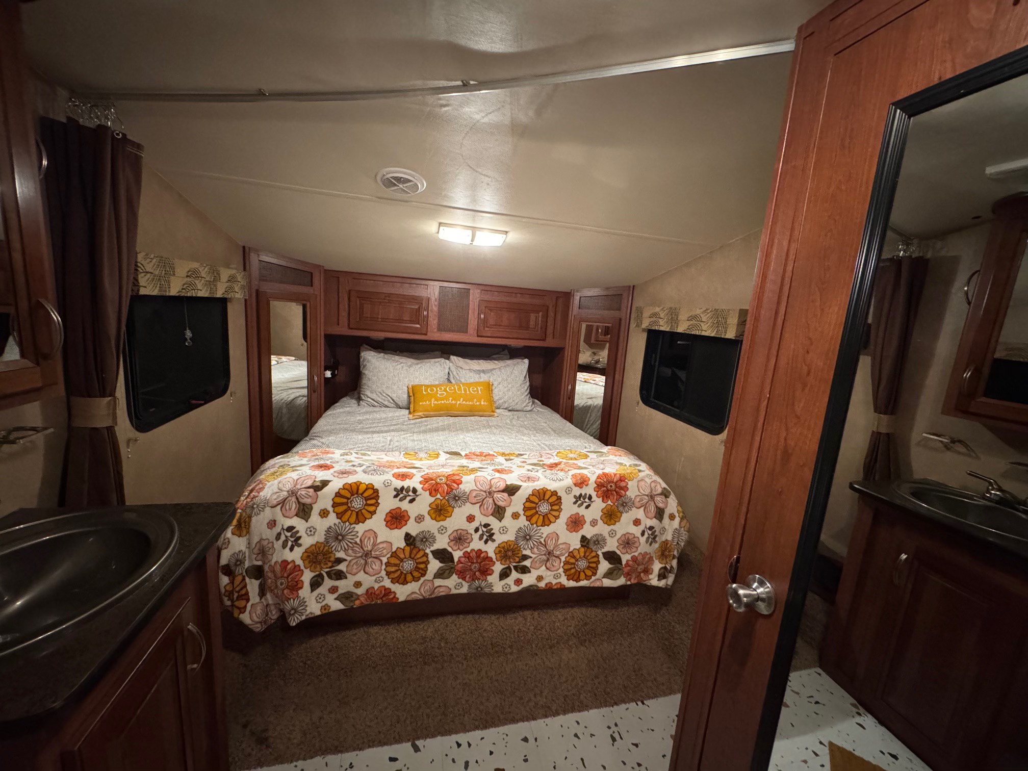 Inside an RV rental: a cozy bedroom with a large bed, floral throw, cabinets, and a sink on the left.. Forest River Wildcat Extralite 2012