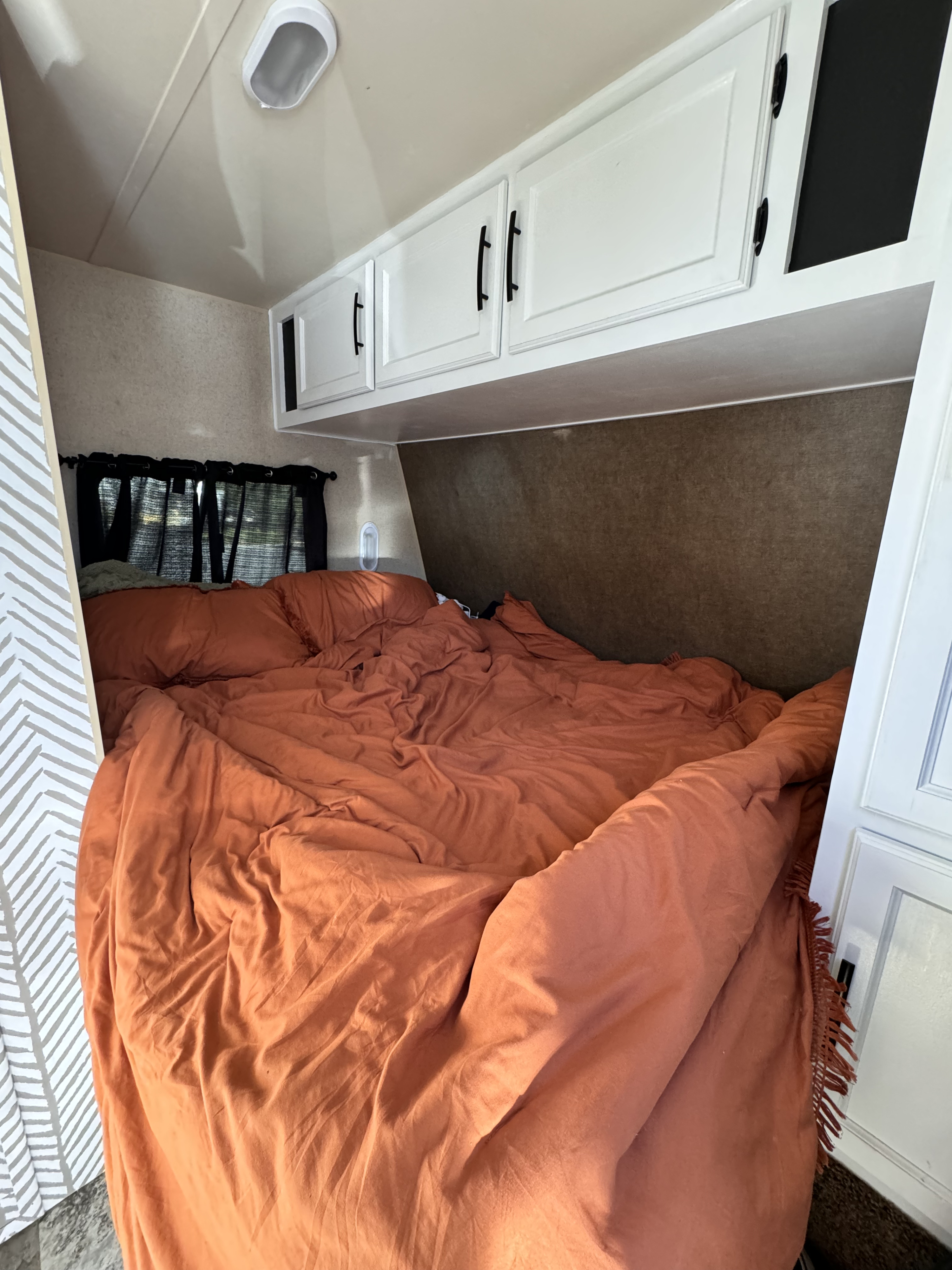 Cozy RV rental bedroom featuring an orange bed, overhead cabinets, & window with curtains.. Jayco Jay Flight 2015