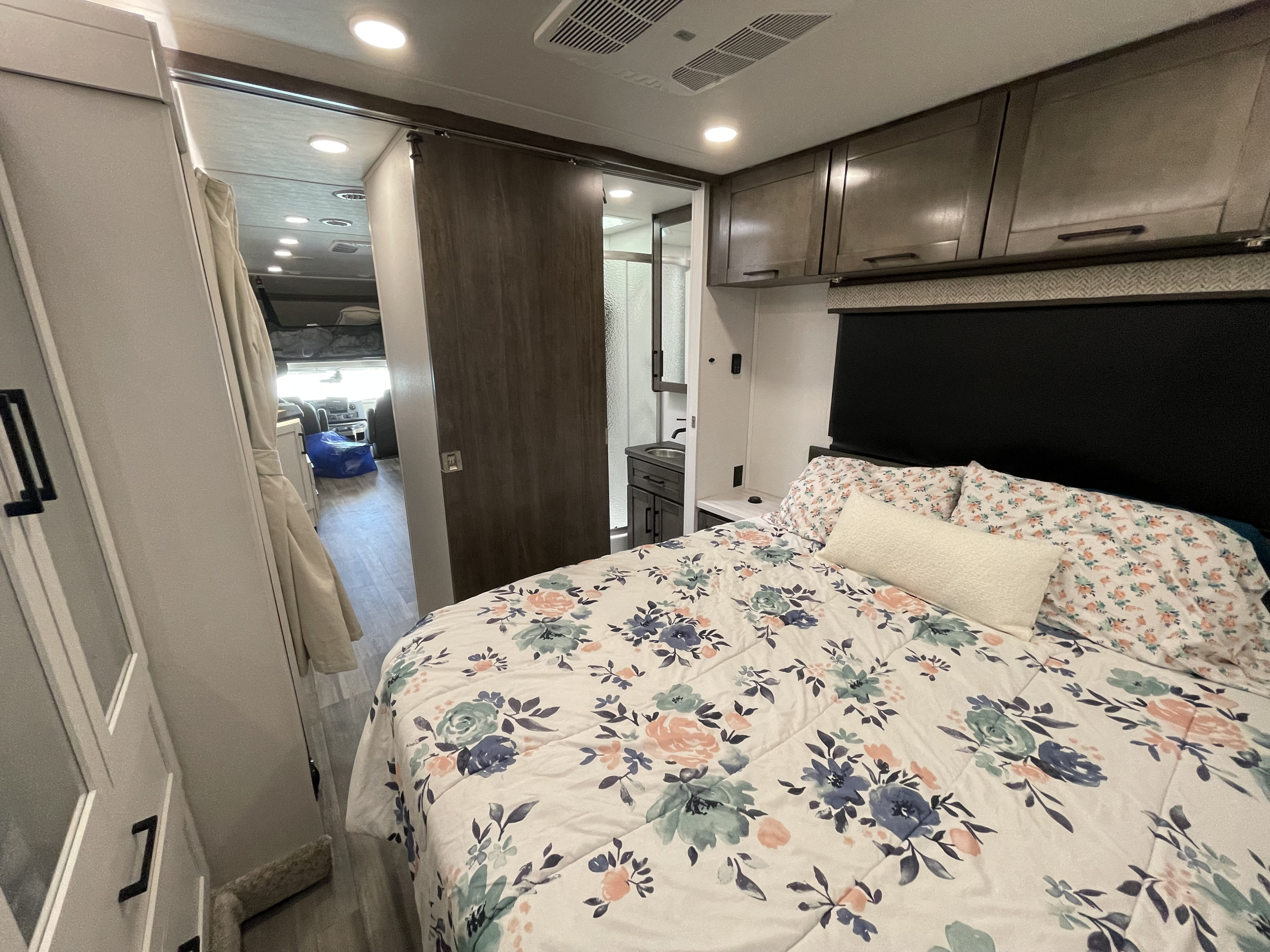 Explore this comfortable RV rental bedroom featuring floral bedding, overhead storage, and access to a compact bathroom.. Jayco Greyhawk 2026