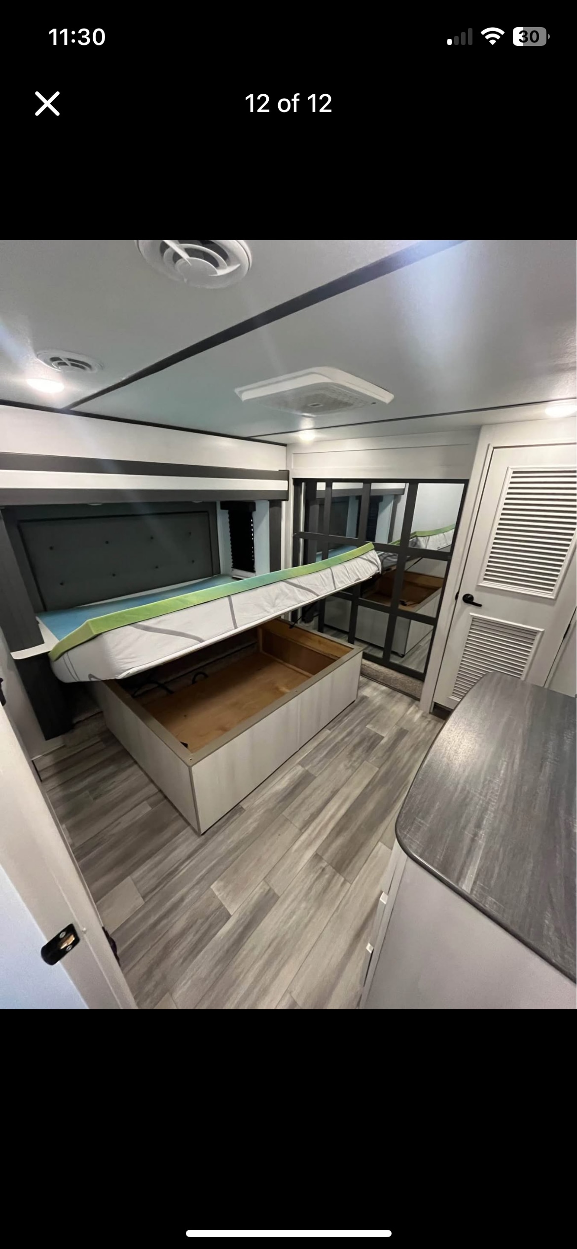 Inside an RV rental bedroom: a lift-up bed reveals ample storage space, with modern grey tones & wood-look floors.. Keystone RV Sprinter 2023