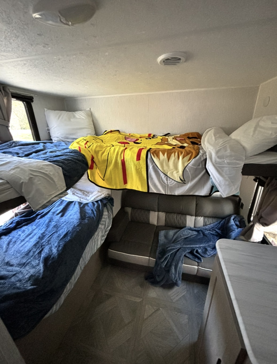 An RV rental's comfy bunk bed setup, featuring a vibrant Pikachu blanket, a lower bed, and a compact seating area.. Forest River Wildwood X-Lite 2024