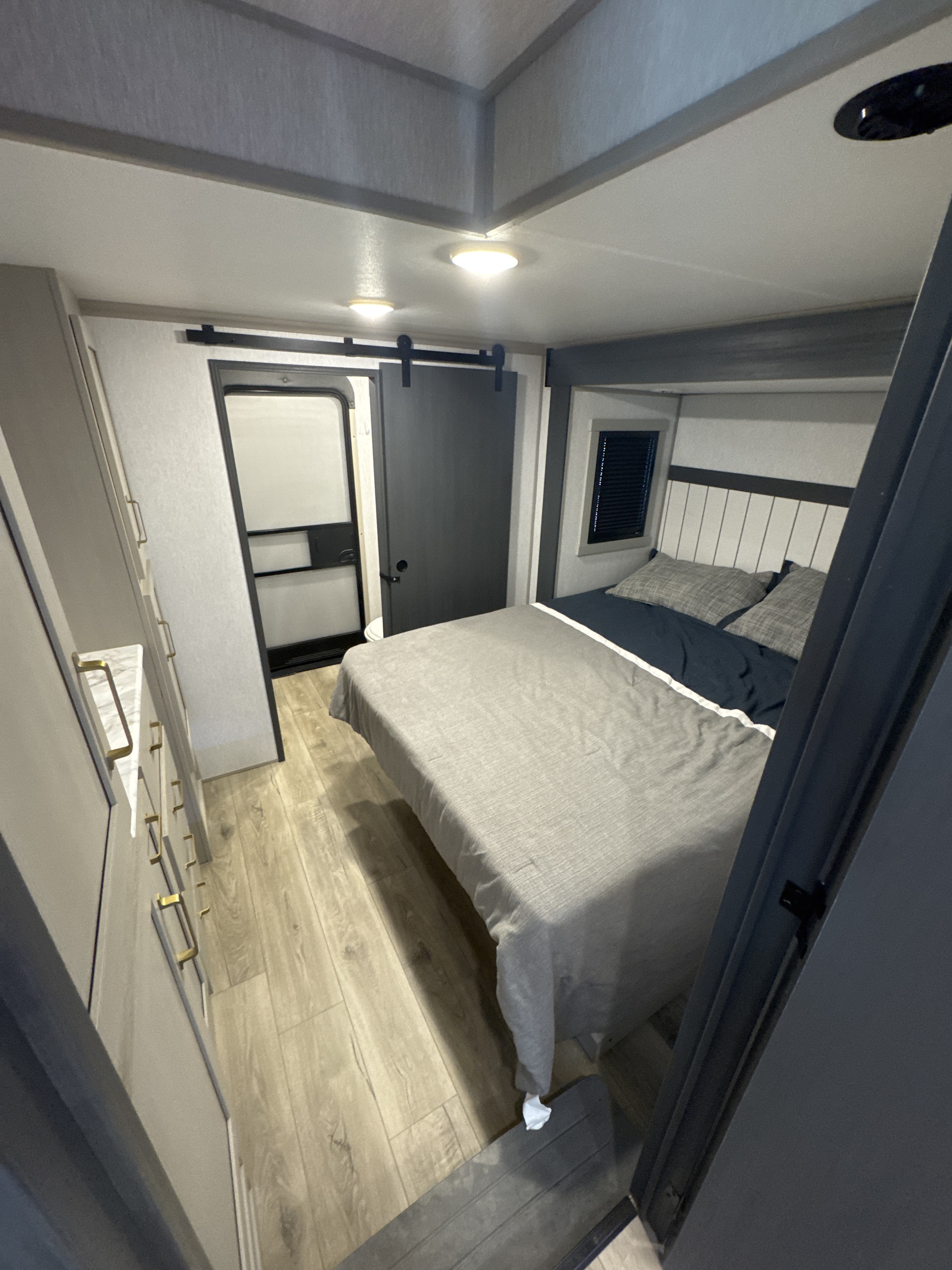 Bright, modern RV rental bedroom with a gray & navy bed, sliding barn door, side storage & window. Ideal for travel.. Forest River Salem Hemisphere 2024