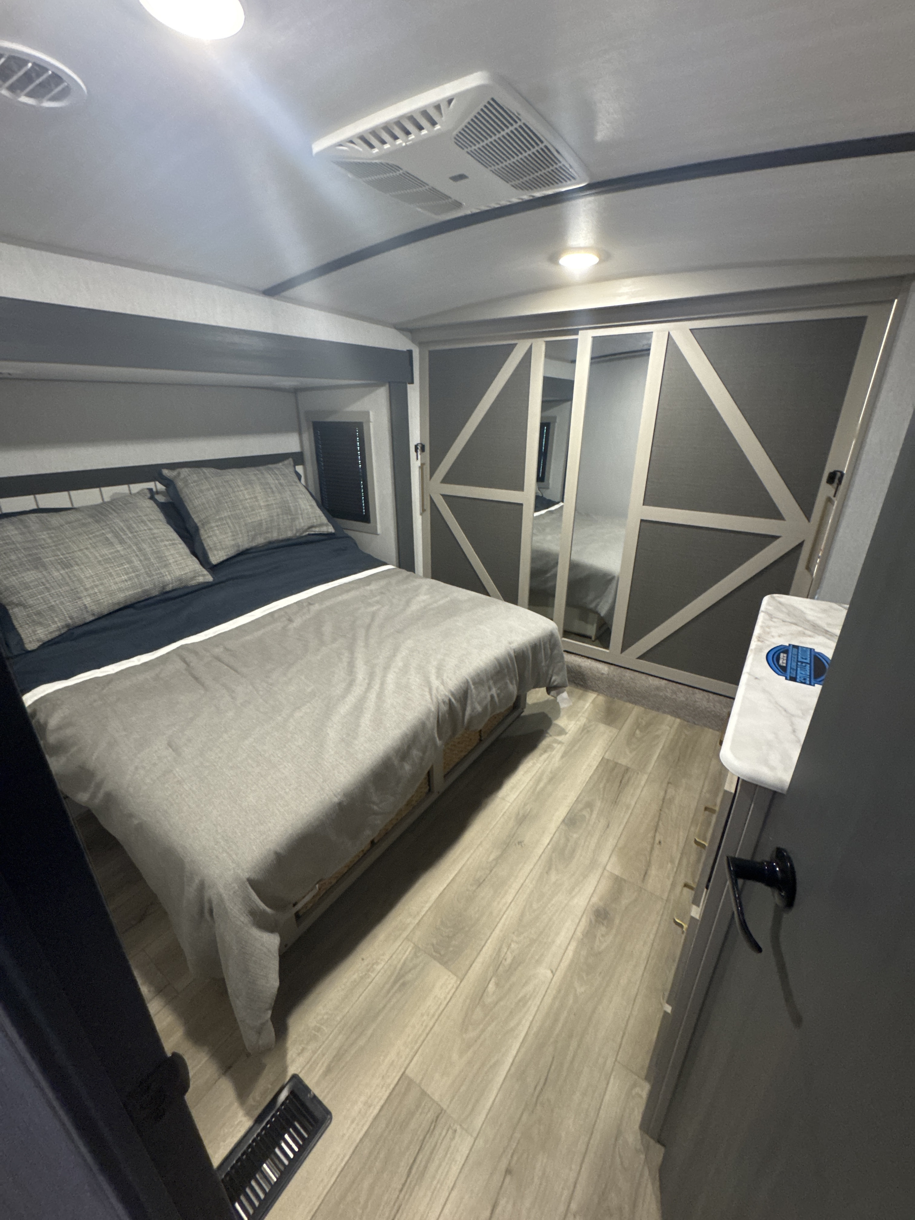 Modern RV rental bedroom: queen bed with grey bedding, overhead AC, and mirrored closets for comfortable travel.. Forest River Salem Hemisphere 2024