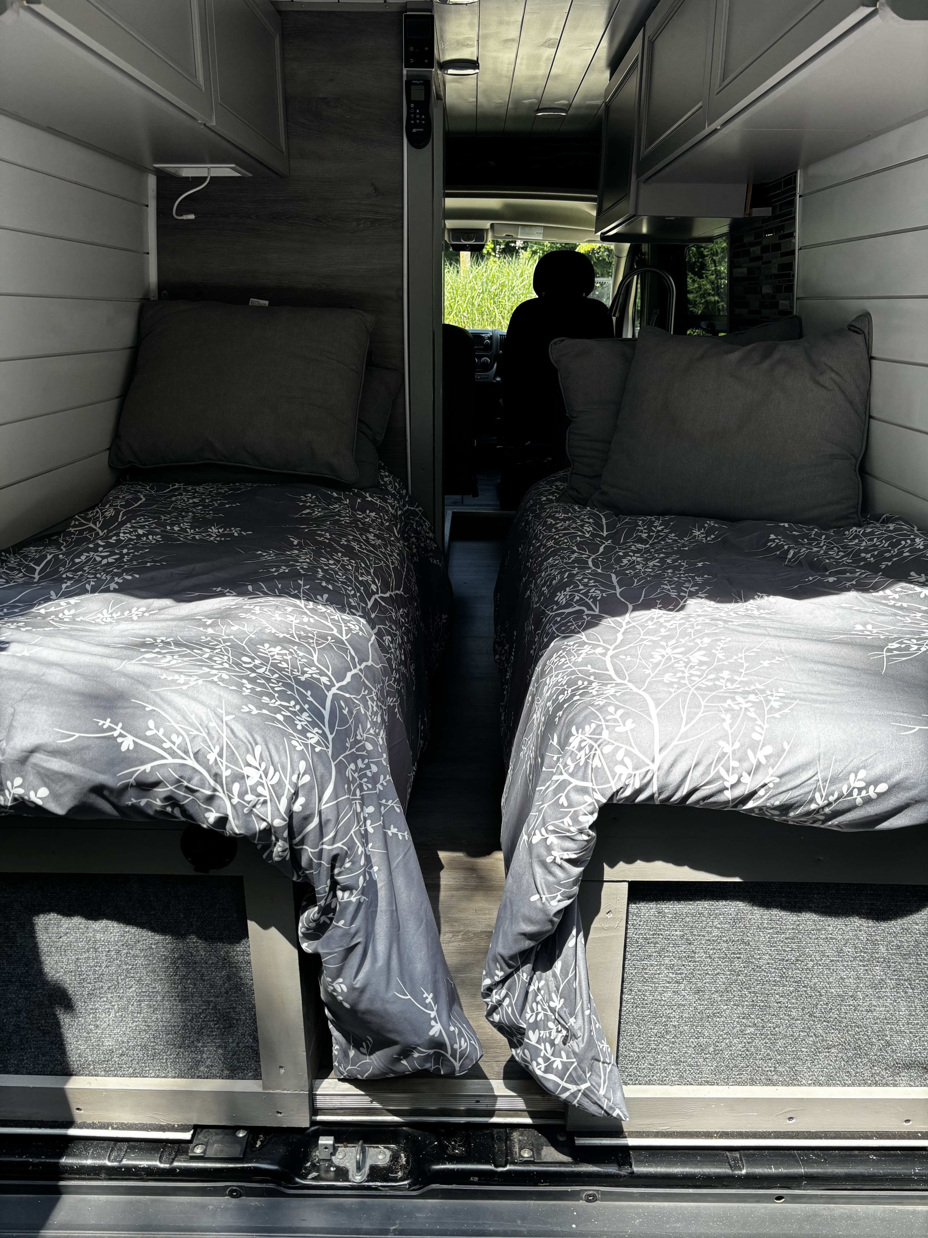 RV rental camper van interior with two comfortable single beds, grey patterned bedding, and narrow aisle leading to the front.. Ram Promaster 2500 High Roof 2016
