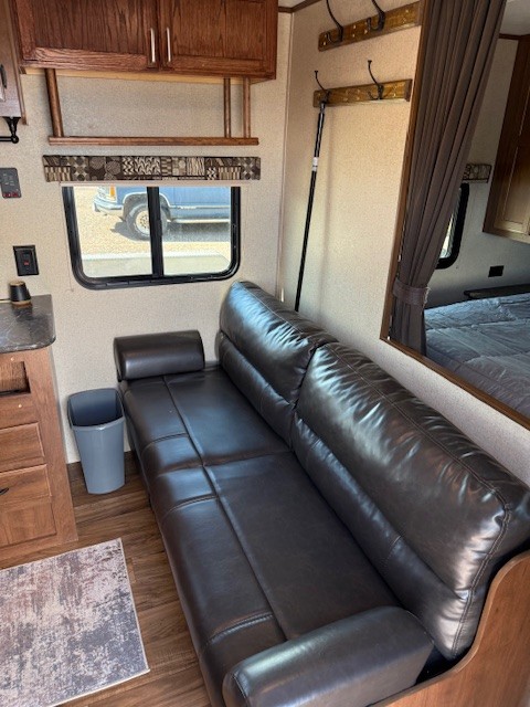Cozy RV rental interior featuring a convertible dark faux leather sofa, wood flooring, window view, and bedroom access.. Jayco Jay Flight SLX 2016