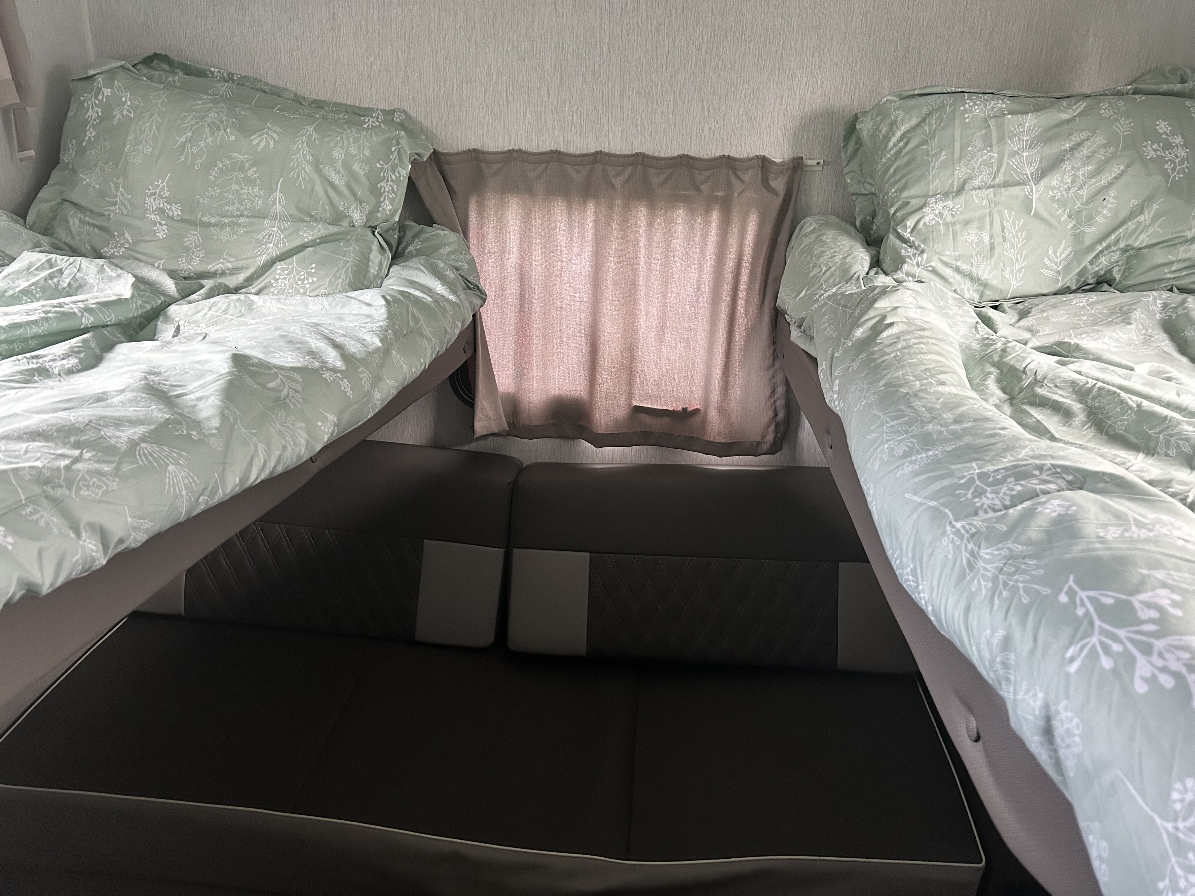 RV rental: Cozy bunk beds with light green floral bedding on both sides, above a dark sofa and a curtained window.. Forest River Salem Cruise Lite 2022