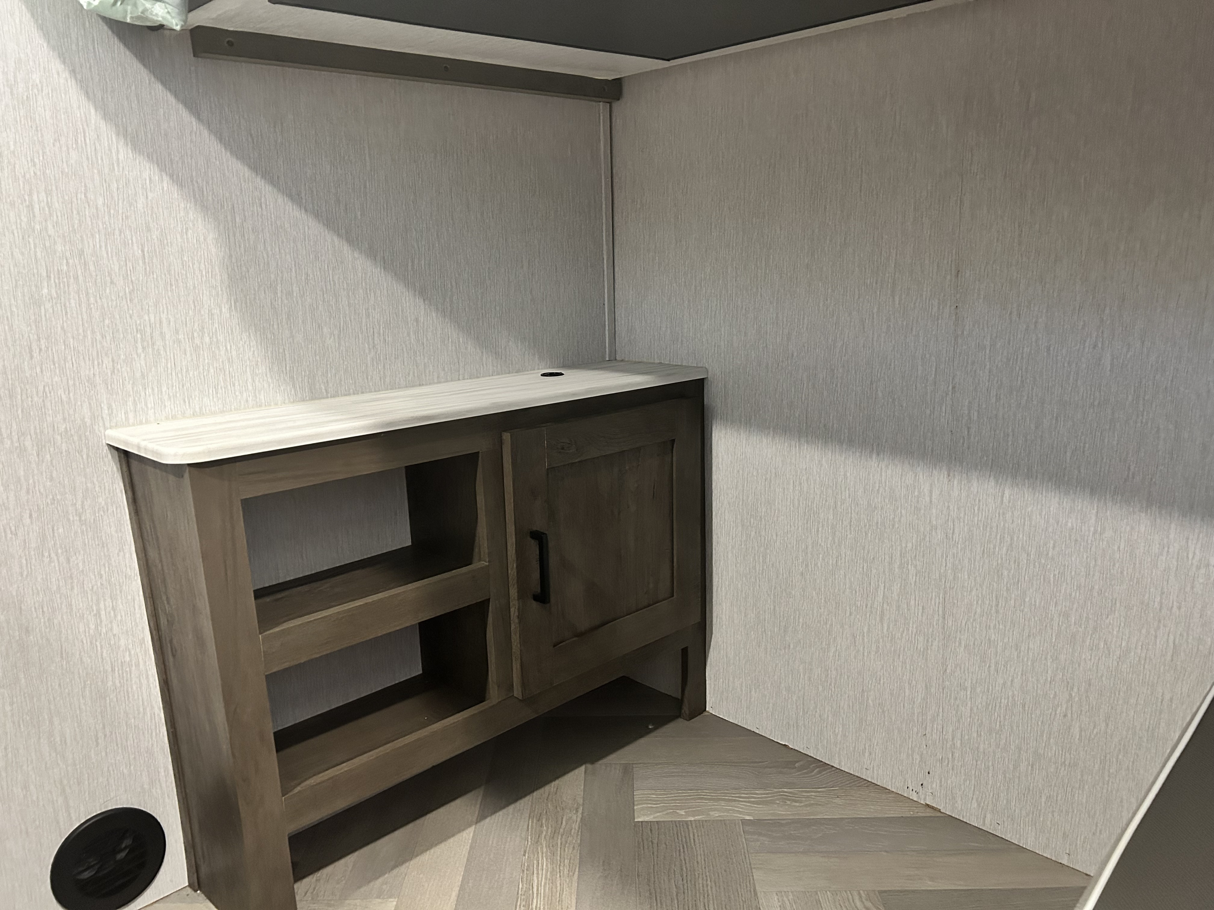Modern RV rental interior with a corner storage cabinet offering shelves and a door, and light wood-look herringbone flooring.. Forest River Salem Cruise Lite 2022