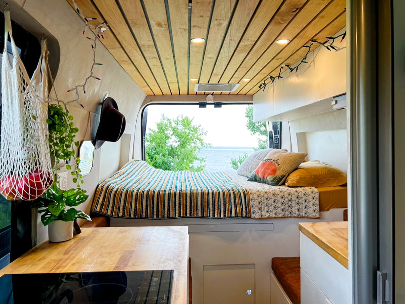 Inside a bright RV rental: a comfy bed with lake view, wood-paneled ceiling, and a compact kitchen counter.. Dodge Ram 1500 2022
