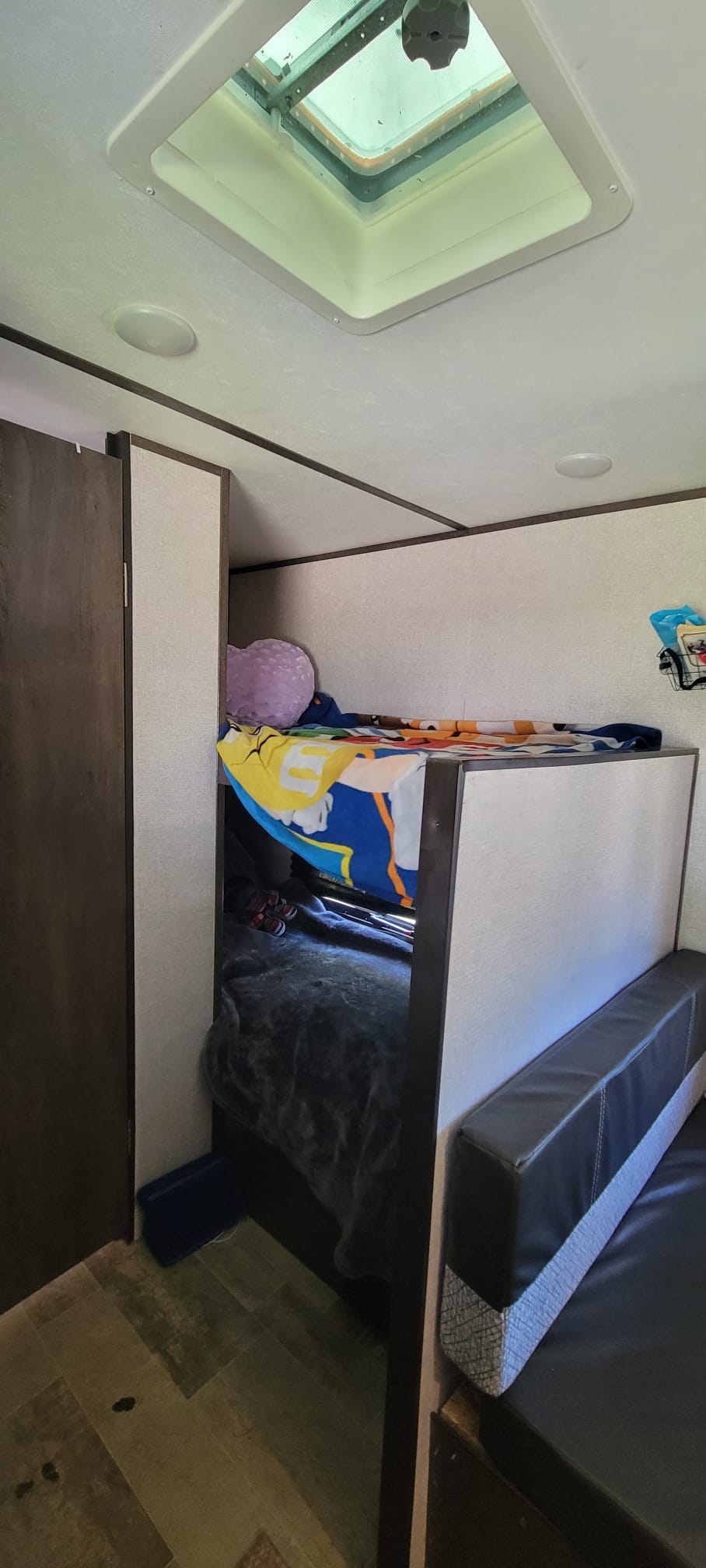 RV rental interior features: a bright skylight, bunk beds with blankets, and a black seating area.. Keystone RV Coleman Lantern 17B 2021