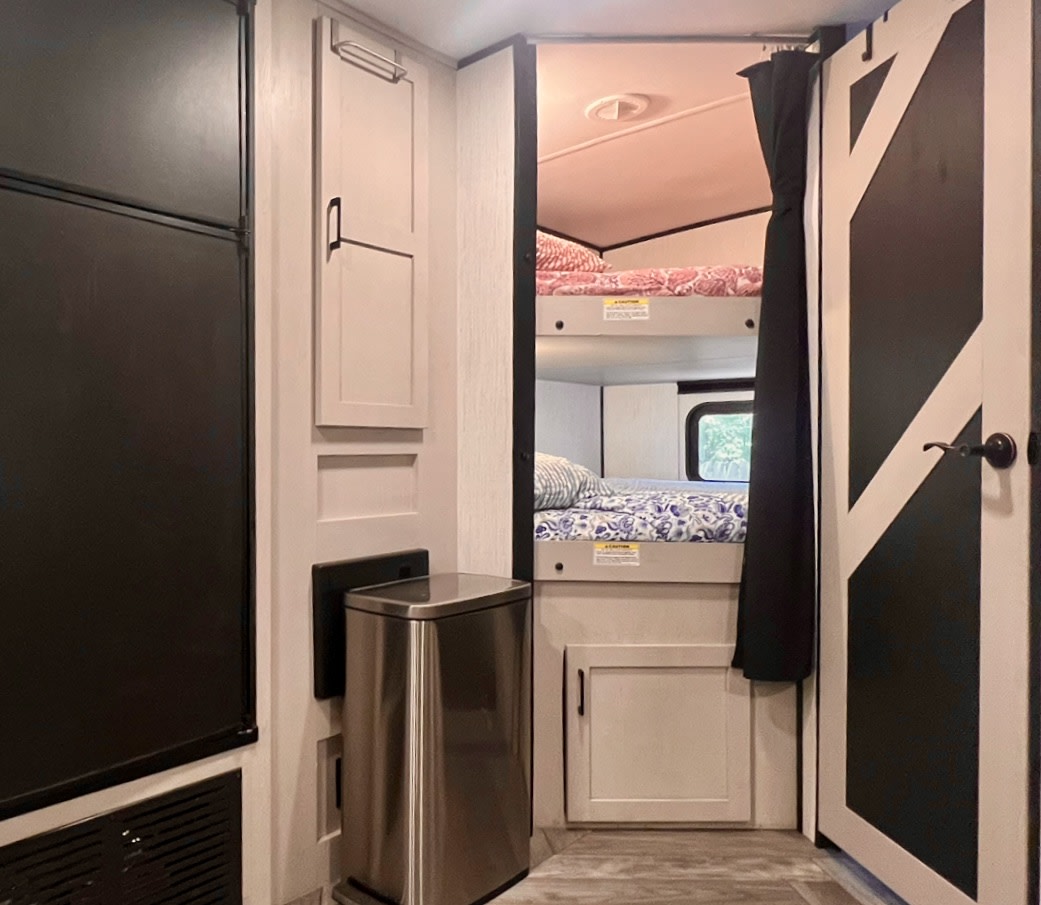 Inside this RV rental: comfy bunk beds with privacy curtains, a large fridge, a sleek trash can, and a barn door. Ready for travel.. Heartland RVs Mallard 2024