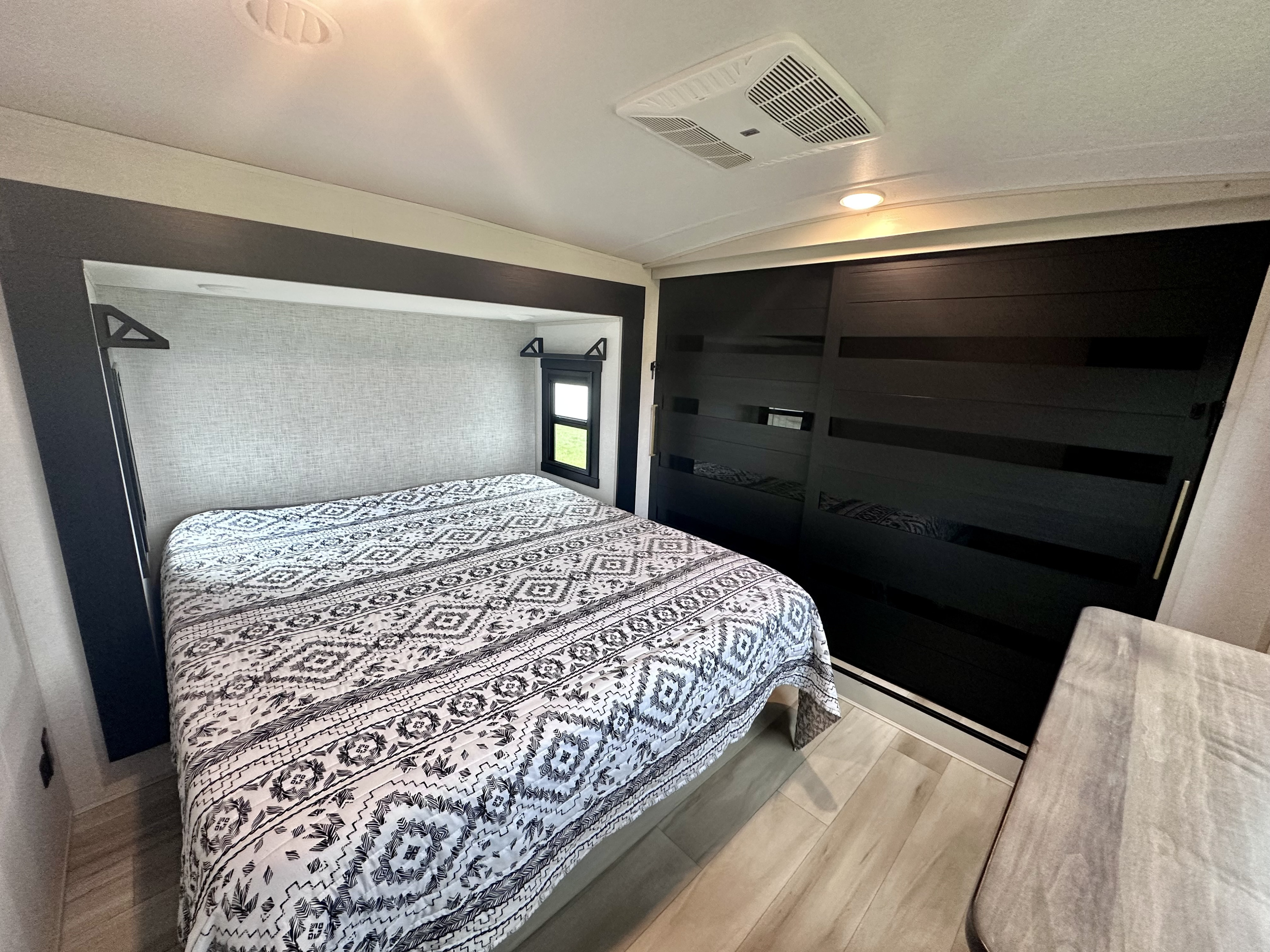 RV rental bedroom interior: bed with patterned comforter, built-in closet, and light wood flooring.. Forest River Heritage Glen 2025