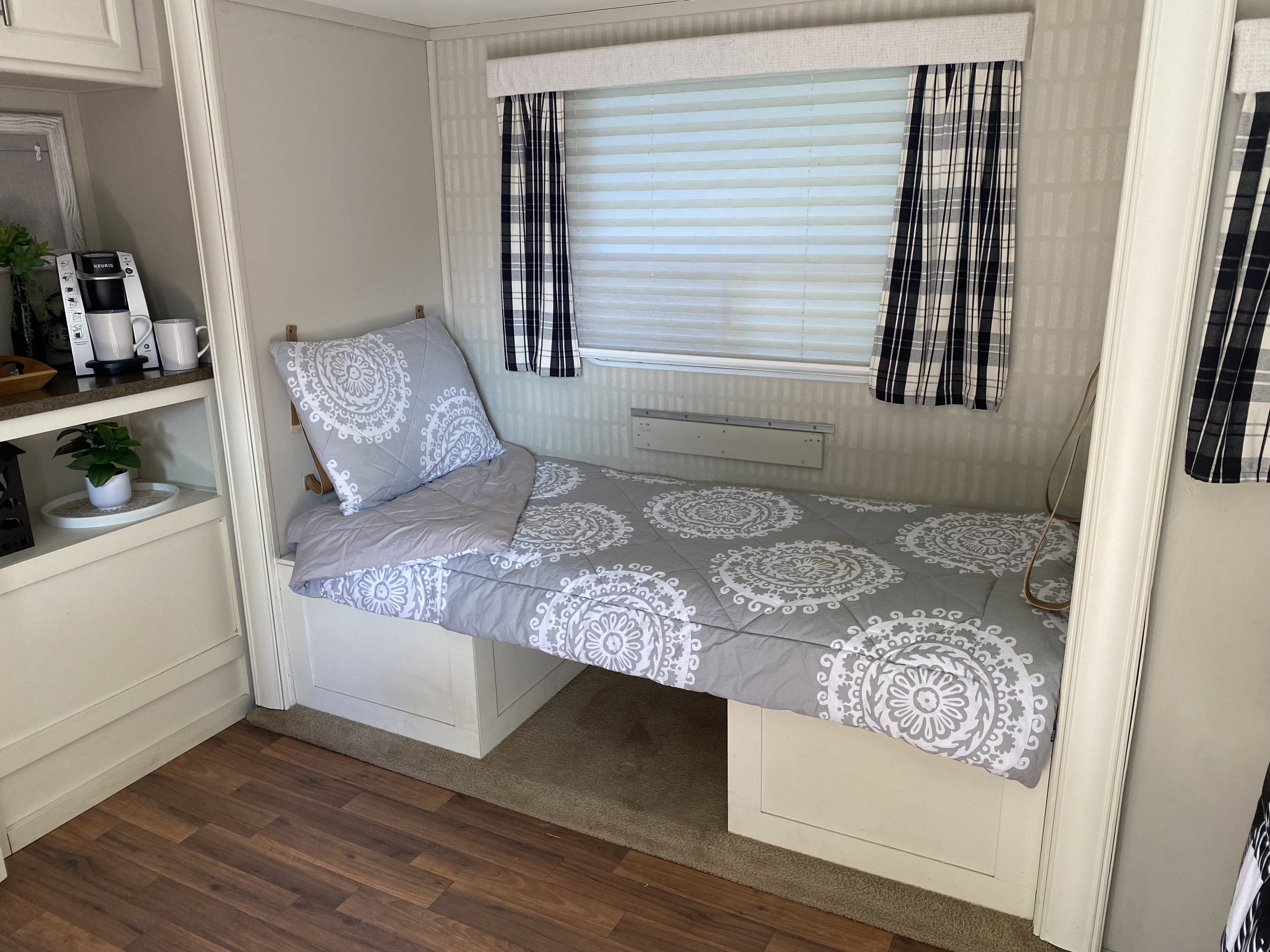 Cozy RV rental interior showing bed with mandala bedding, a window with blinds, and a coffee station.. Cruiser RV Fun Finder X 2011