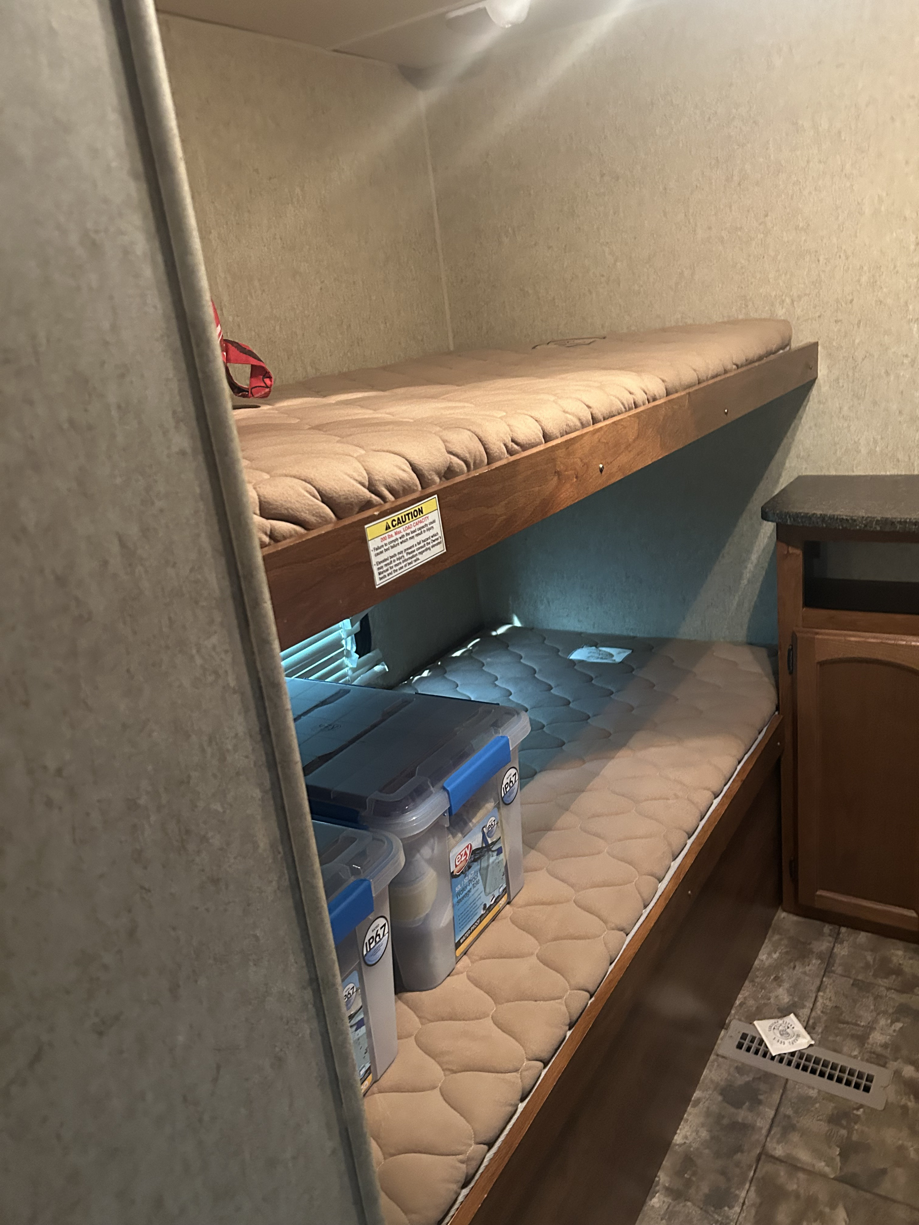 Inside an RV rental: cozy bunk beds with storage containers, a caution sign, and a floor vent visible.. Heartland Trail Runner 2013