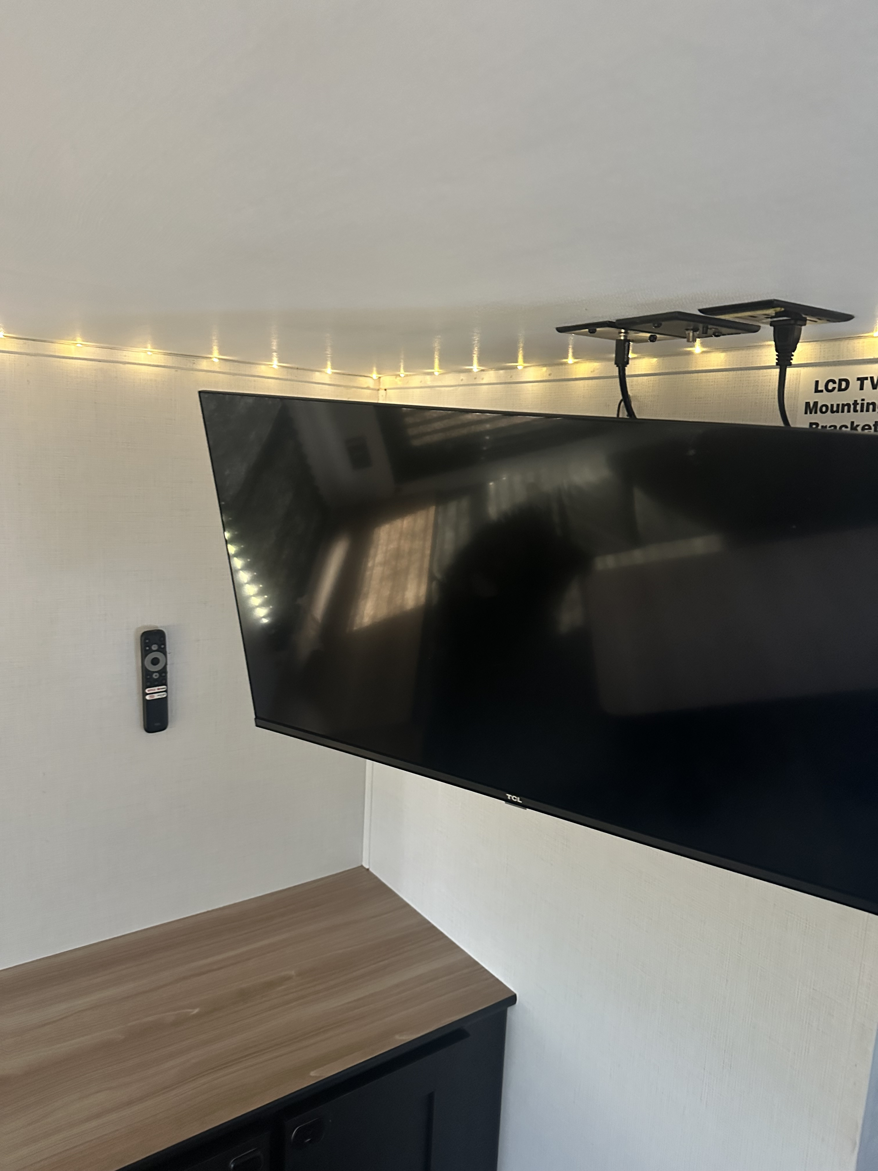 Compact RV rental interior with a ceiling-mounted TCL TV, wall-mounted remote, decorative LED lights, and wooden cabinet.. Keystone RV Springdale 2022