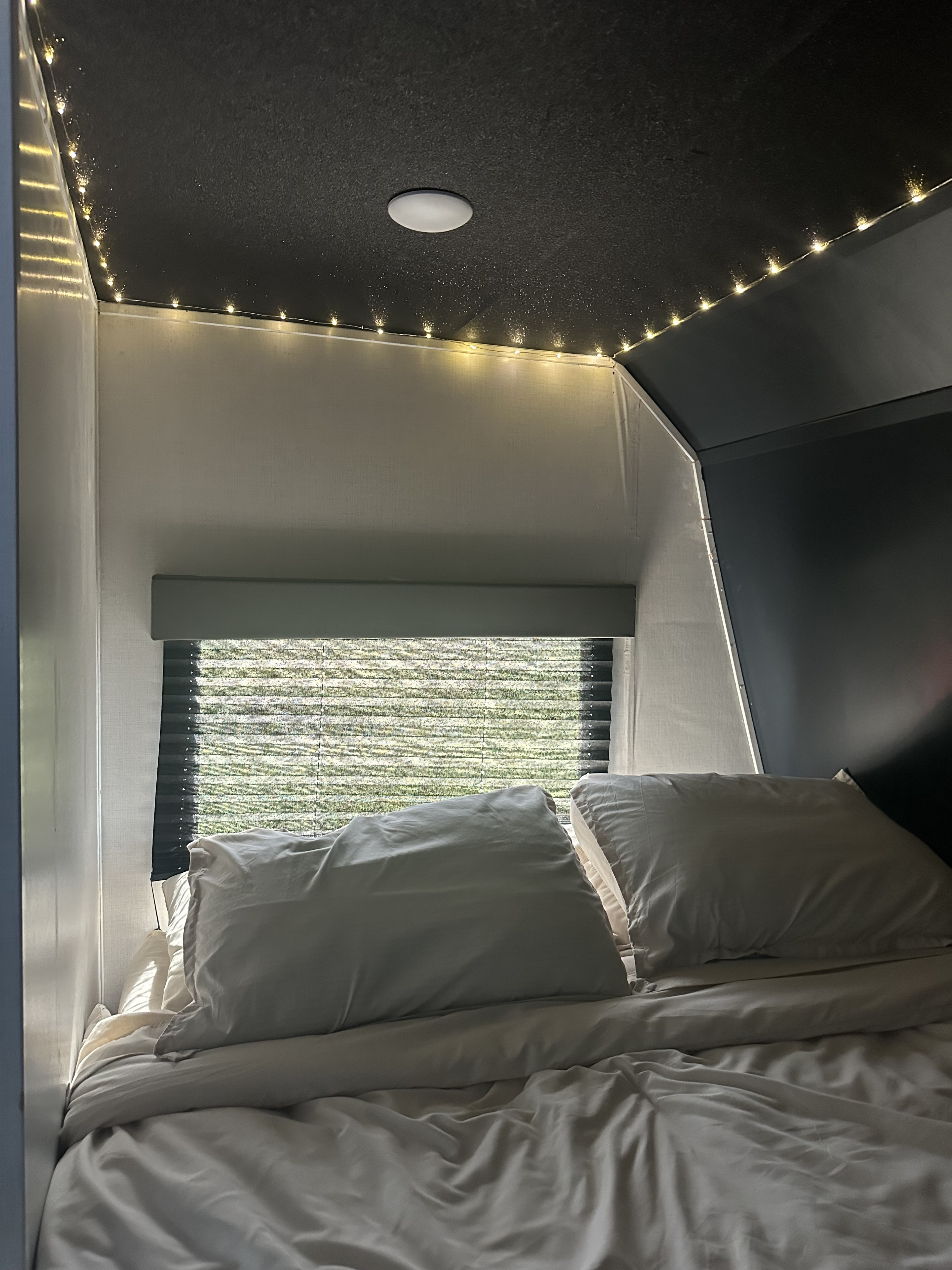 Cozy RV rental bedroom interior: comfy bed, window view of nature, and ambient string lights on the dark ceiling.. Keystone RV Springdale 2022