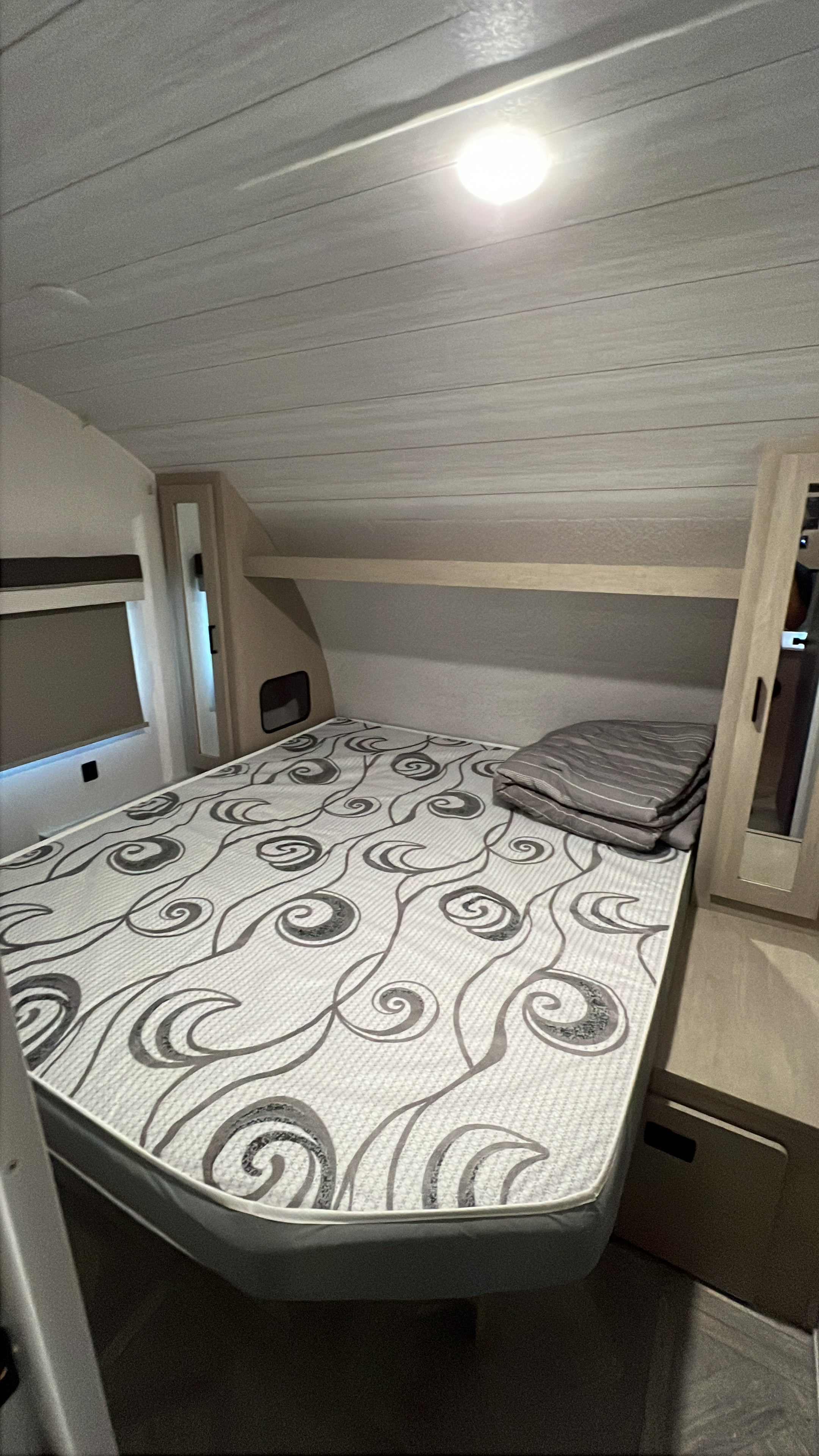 Compact RV rental bedroom interior featuring a patterned bed, overhead shelf, and window with blinds.. Forest River Salem Cruise Lite 2023