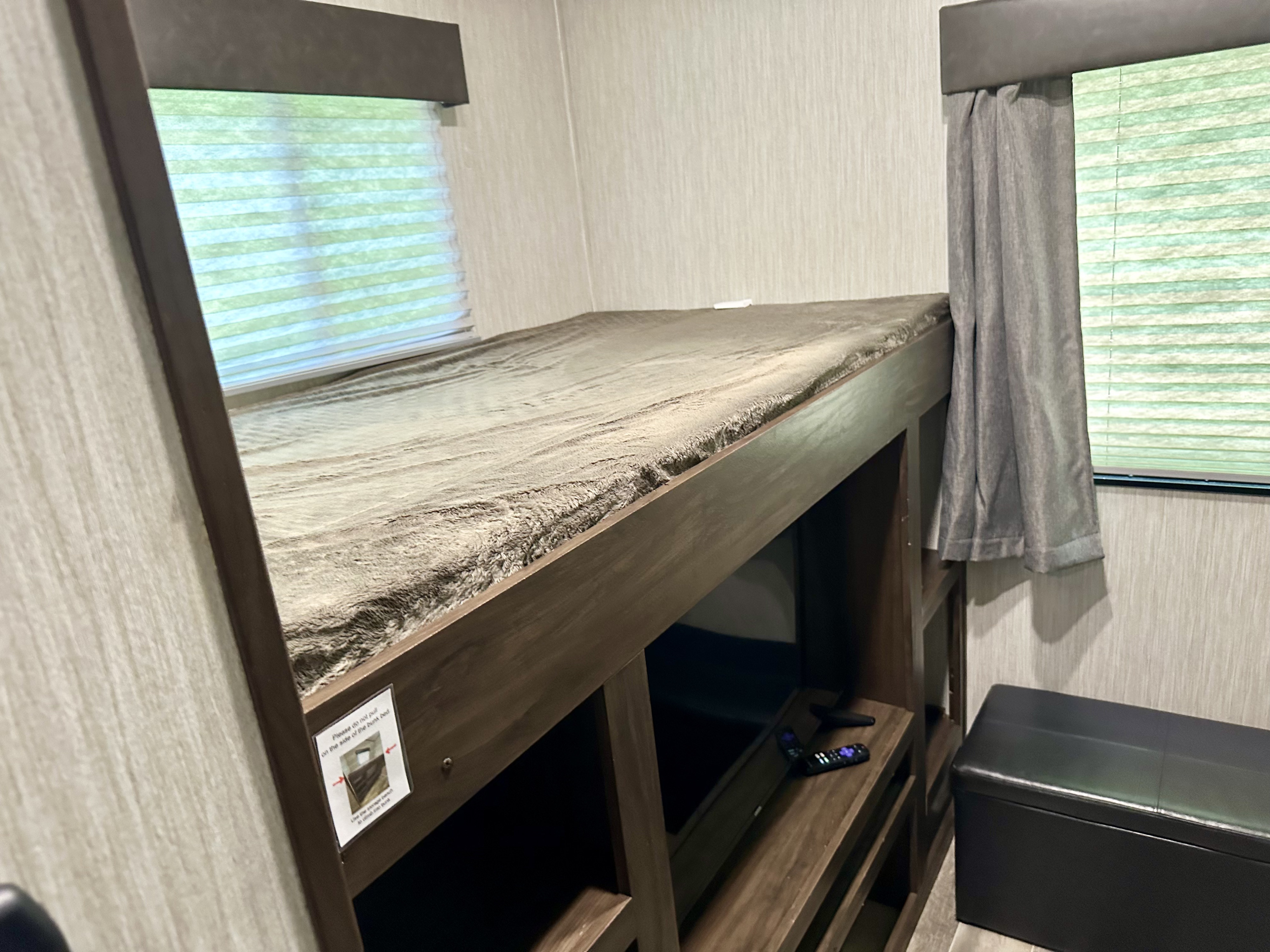 This RV rental bunk room offers a comfy upper bunk, built-in TV, and a black storage ottoman, perfect for families.. Forest River Cherokee Arctic Wolf 2019