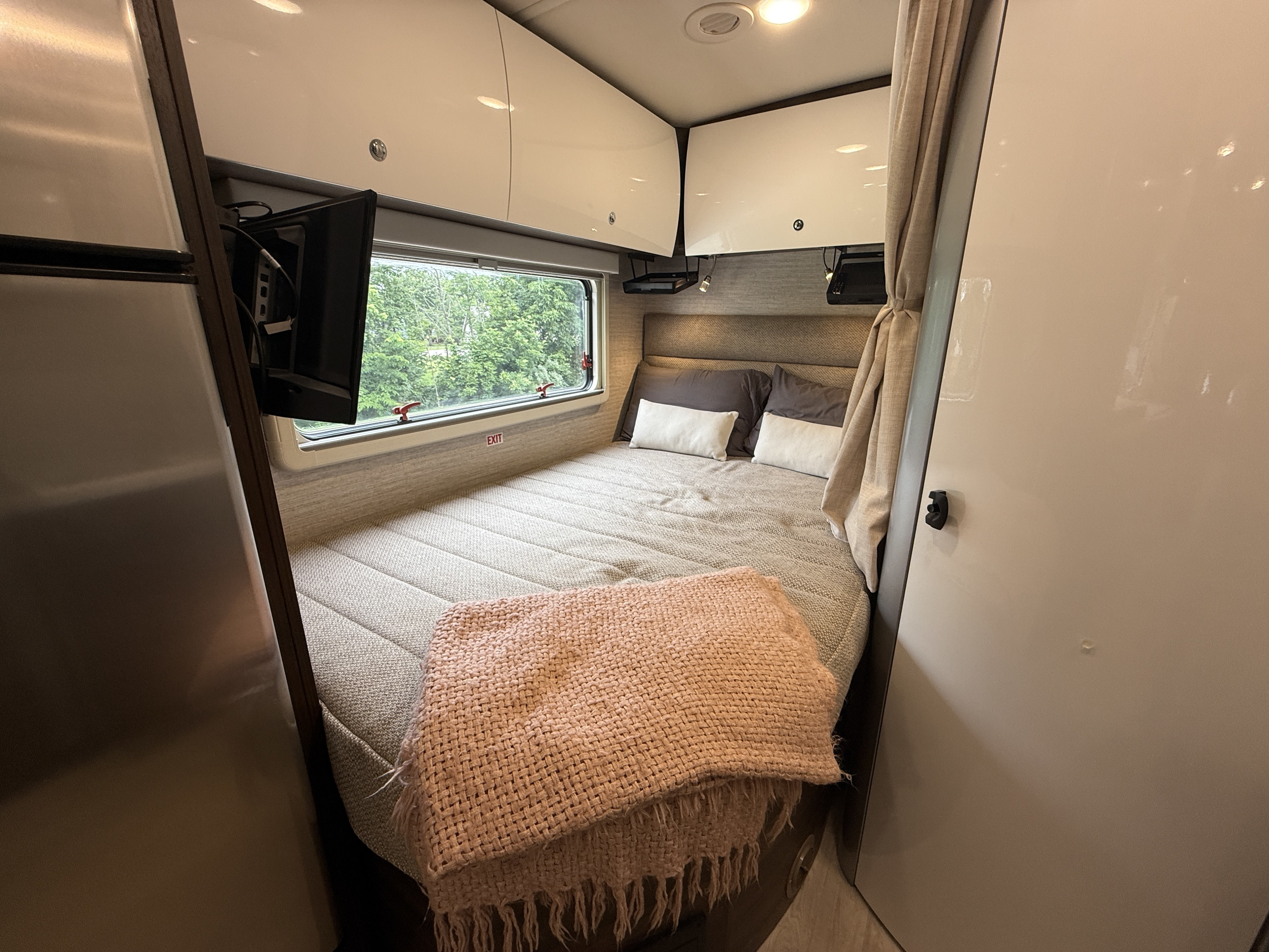 Cozy RV rental bedroom with a comfy bed, window view, and TV for a relaxing journey.. Winnebago View 2022