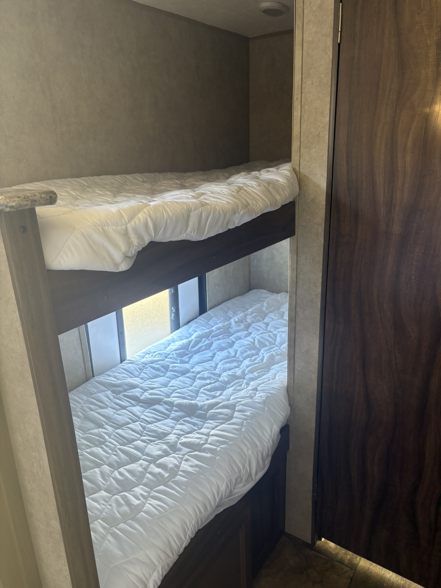 Comfortable bunk beds in an RV rental, ready for your next adventure. White quilted bedding with natural light from a window.. Forest River Viking 2016