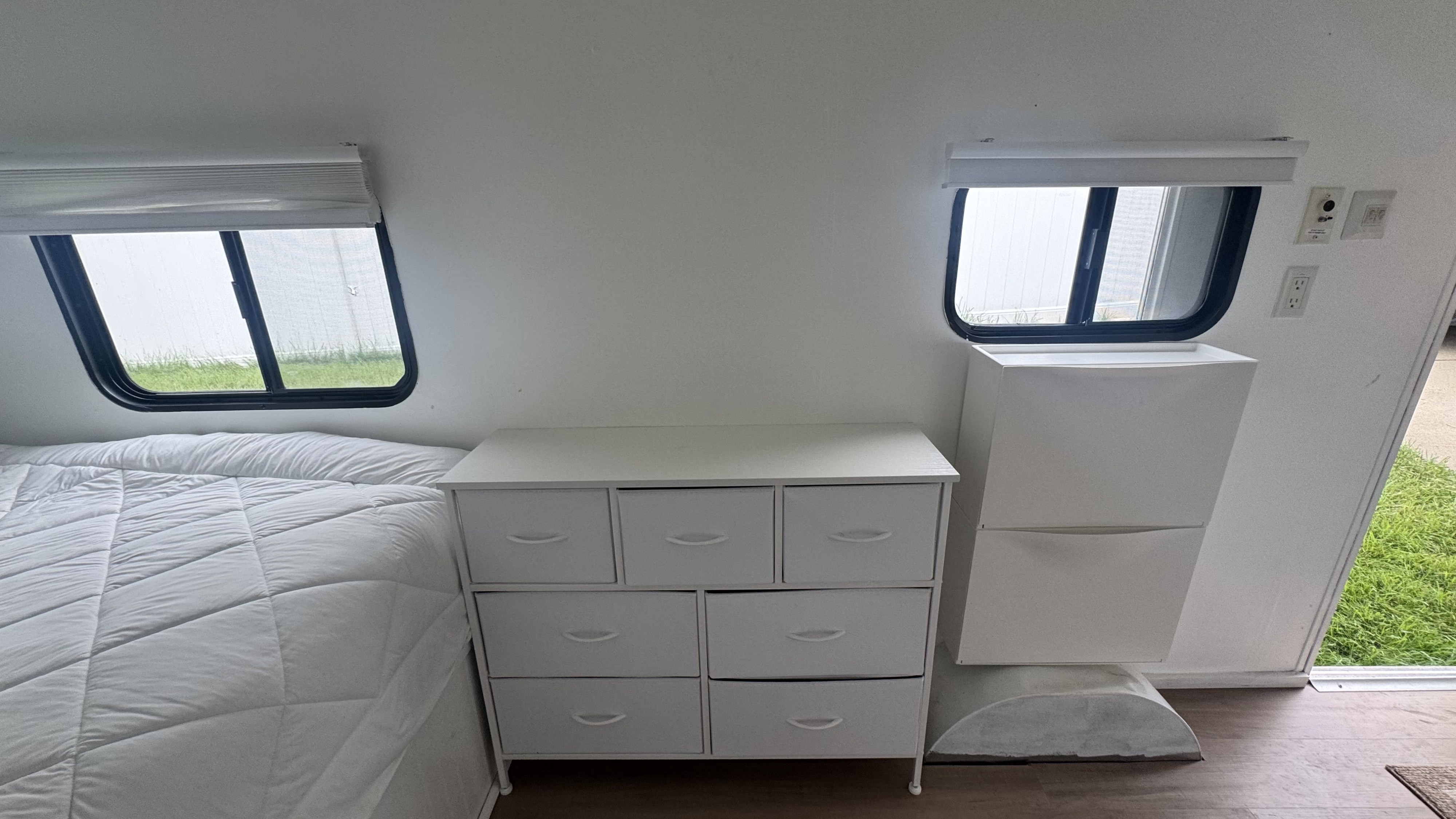 Clean white RV rental bedroom features a bed, fabric-drawer dresser, tall storage unit, windows, and wood floor.. Jayco Jay Flight Swift SLX 2013