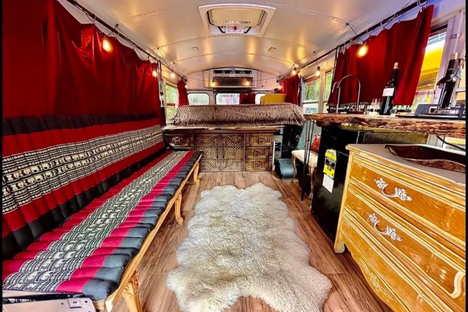 Step into this bohemian-chic converted bus interior, available for RV rental. Features a cozy bed, patterned cushions, and antique-style furnishings.. Ford F450 2008