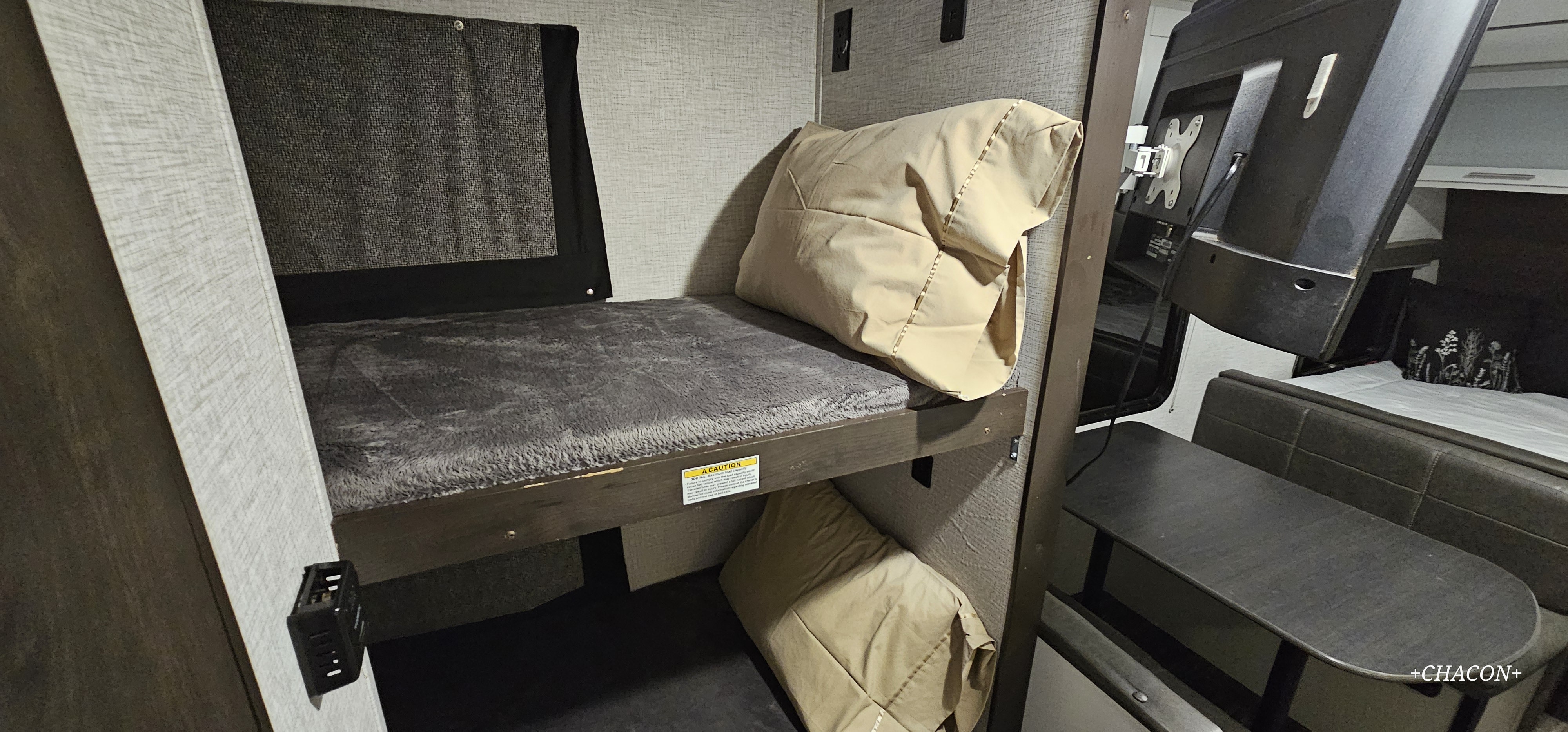 RV rental bunk room: upper bed with grey blanket, lower sleeping area, and a dinette with a mounted TV. Efficient use of space.. Keystone RV Bullet Crossfire 2021