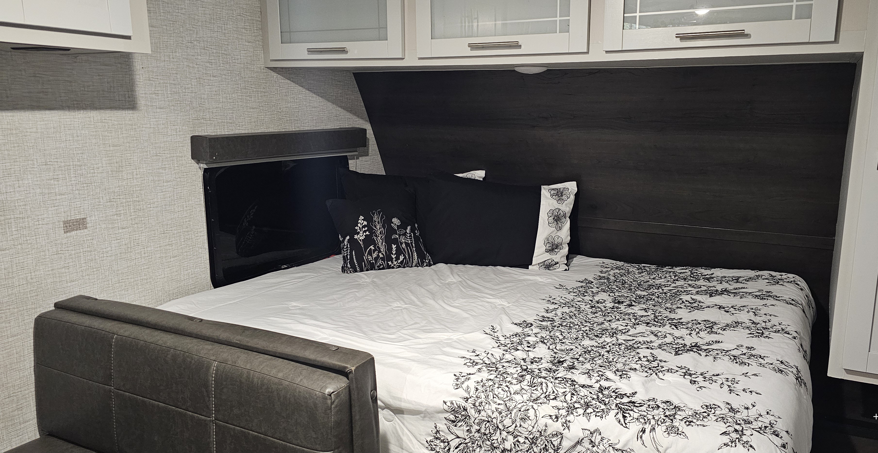 Cozy RV rental bedroom featuring a bed with elegant floral bedding, dark wood accents, and overhead cabinets.. Keystone RV Bullet Crossfire 2021