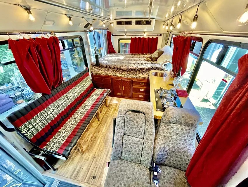 Cozy custom RV rental interior with a bed, compact kitchen, lounge sofa, and two passenger seats, designed for comfort.. Chevrolet Express 3500 2015