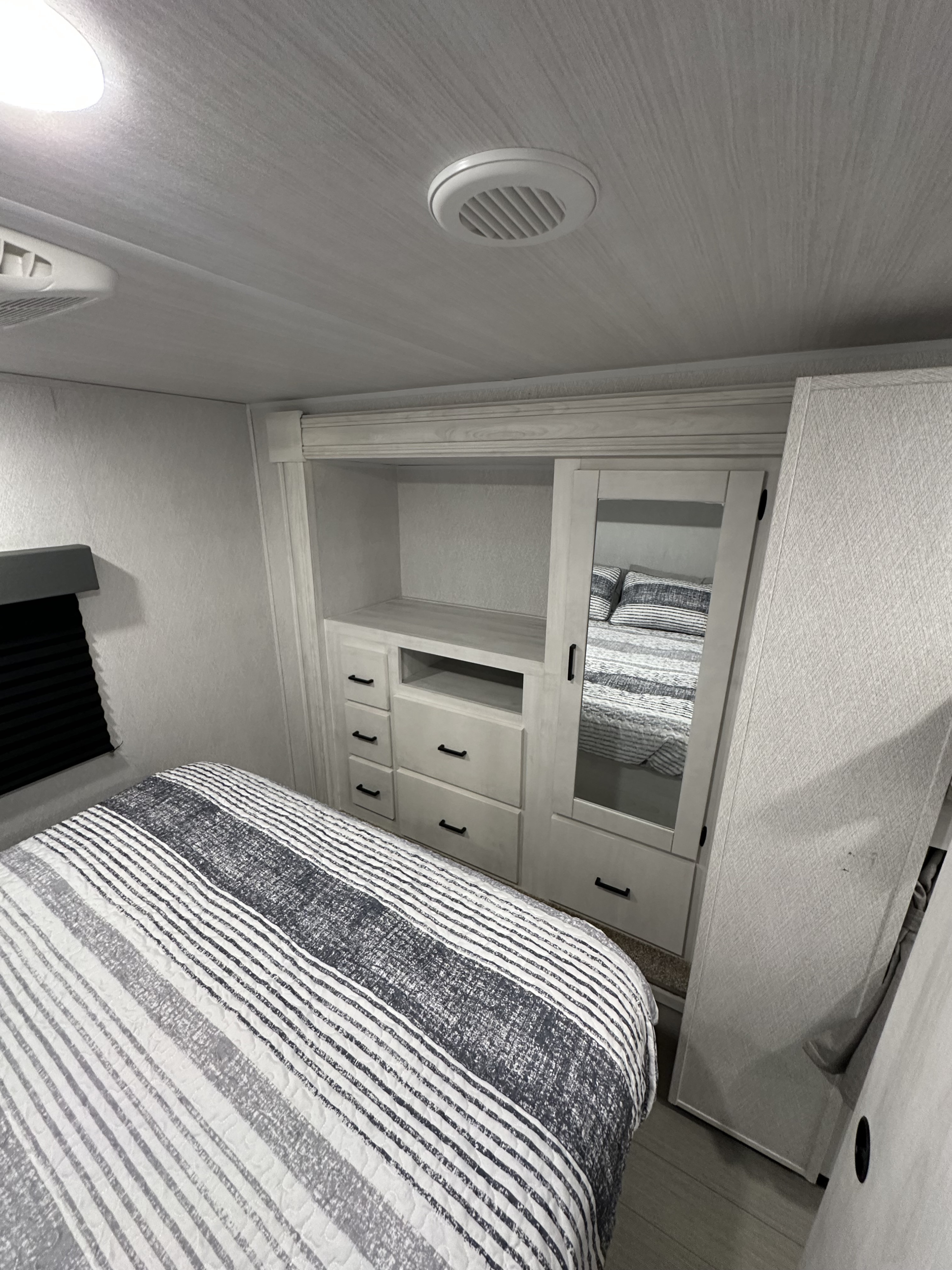Modern RV rental bedroom: cozy bed with striped bedding, built-in storage, and mirrored closet for travel.. East to West Entrada 3100FB 2025