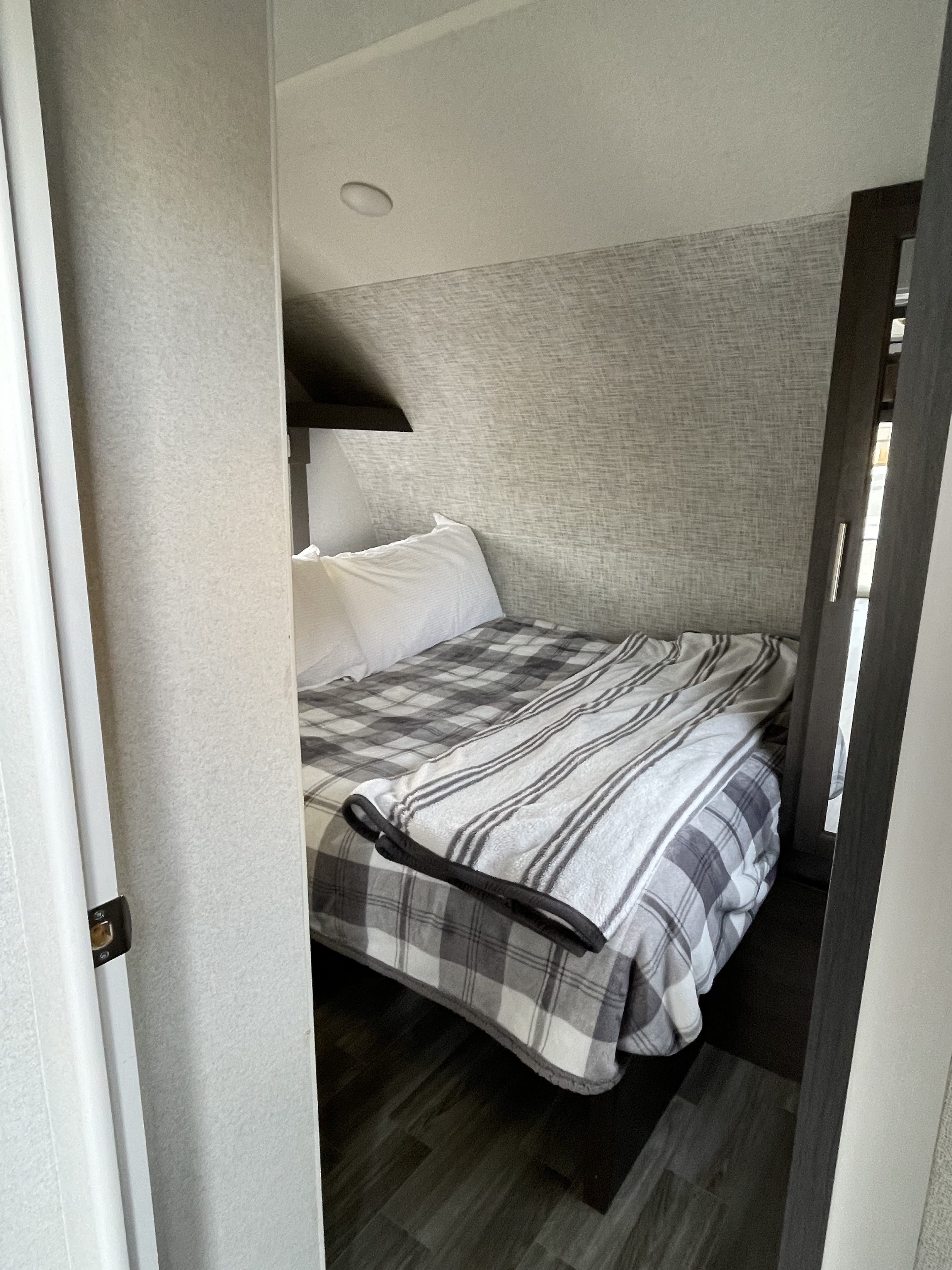 Inside an rv rental: a compact sleeping nook with a cozy bed, plaid bedding, white pillows, and ceiling light.. Forest River Cruise Lite 2020