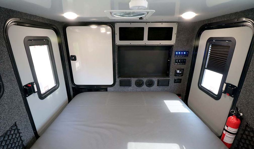 Cozy RV rental interior with a comfortable bed, functional doors, and an entertainment console for travel adventure.. Encore RV ROG 2022