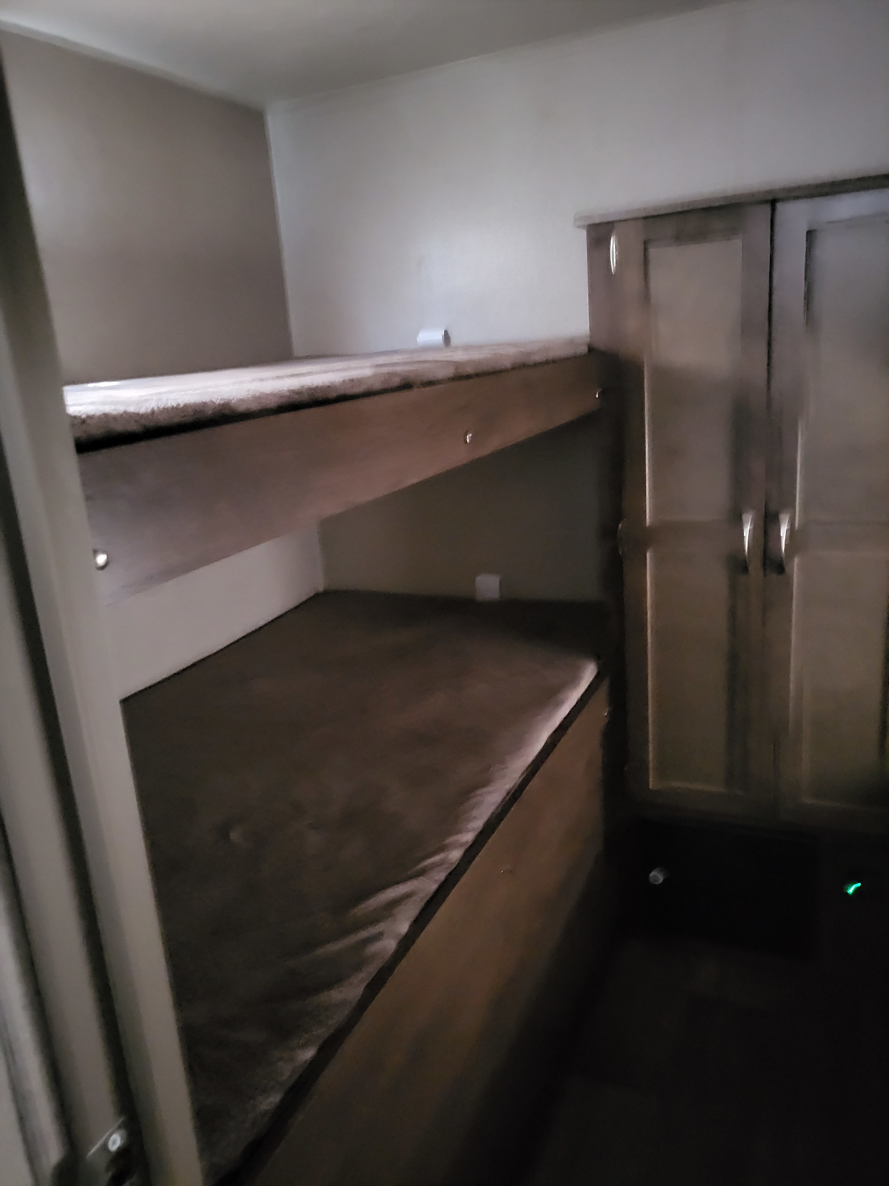 An RV rental's compact interior features two stacked bunk beds with soft mattresses and a tall wooden cabinet on the right.. Forest River Palomino Puma 2018