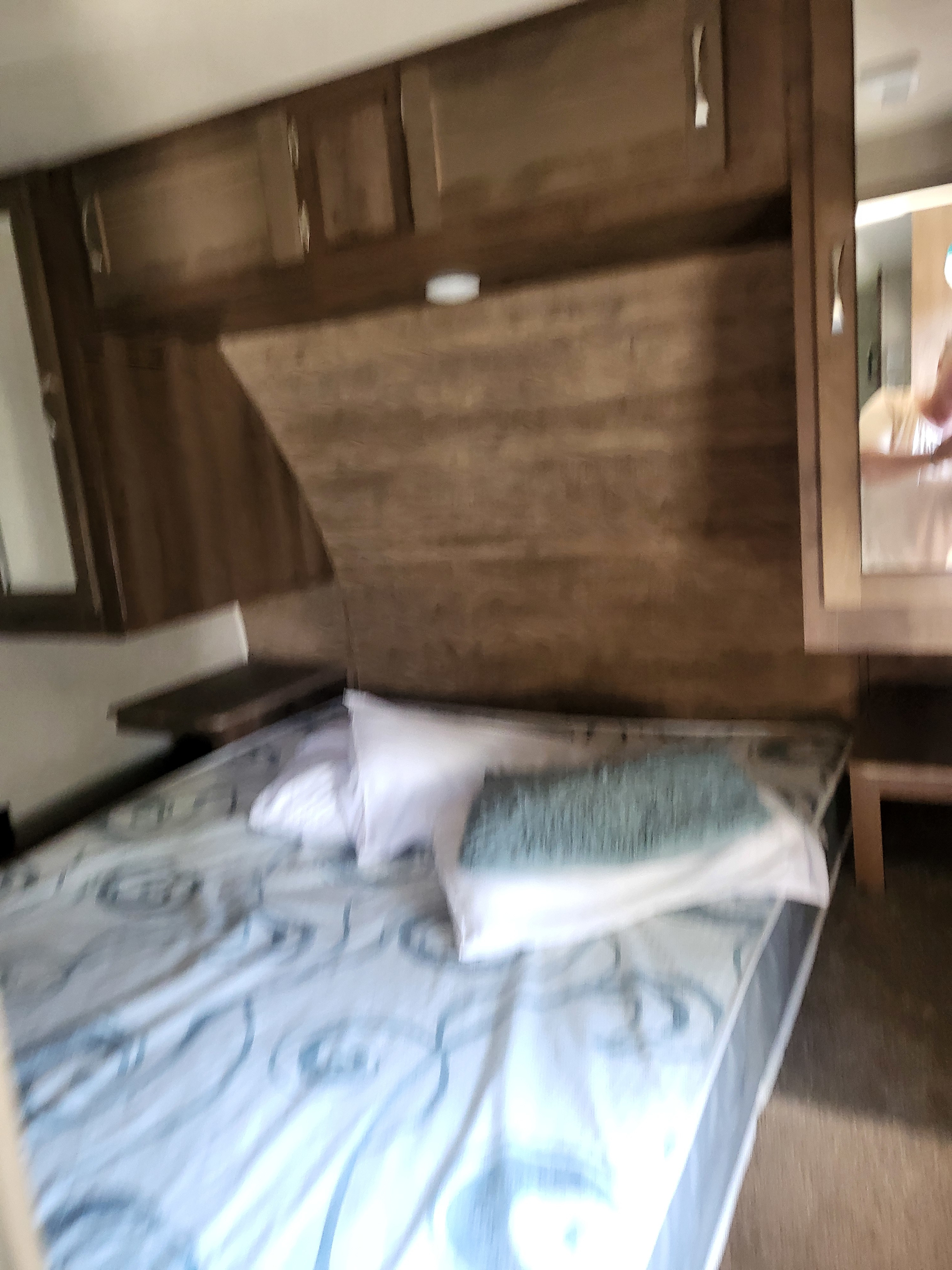 Cozy RV rental bedroom features a bed with white and teal pillows, and wooden overhead cabinets.. Forest River Palomino Puma 2018