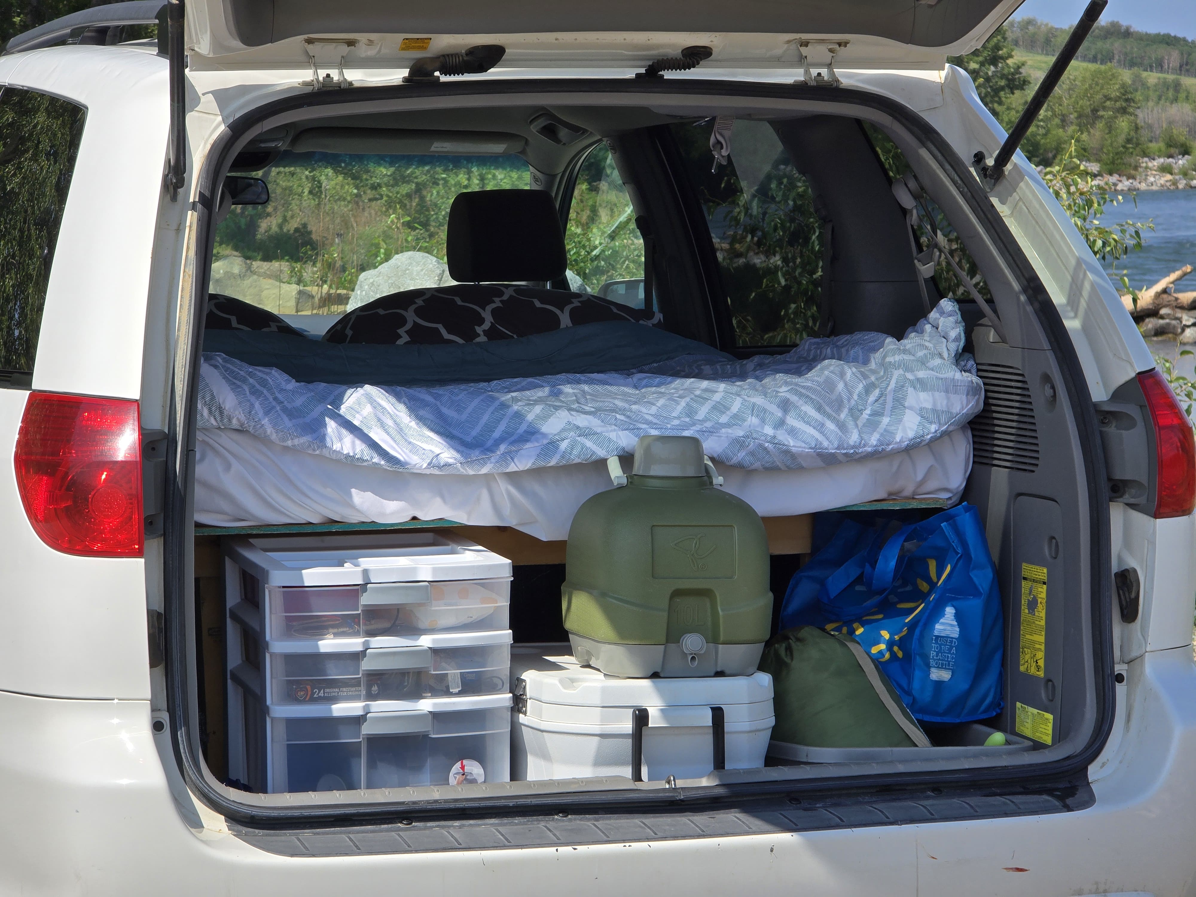 SUV setup like an RV rental: tailgate open, revealing a cozy bed, plastic storage drawers, and camping gear inside.. Toyota Sienna 2007