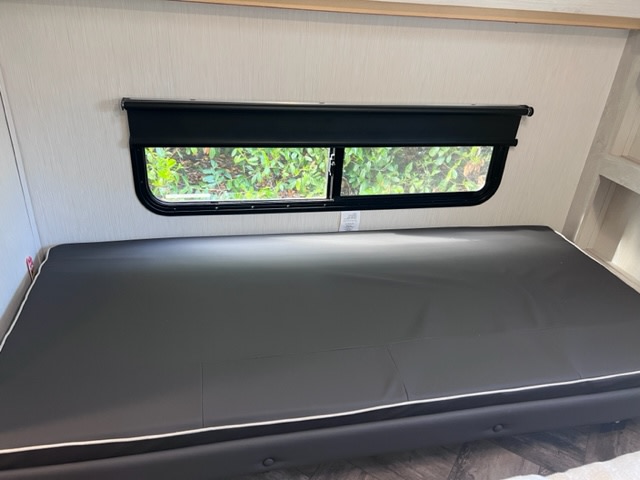 RV rental: Dark, comfortable bed/dinette cushion with white piping beneath a window and shade.. Forest River Wildcat 176BHX 2023