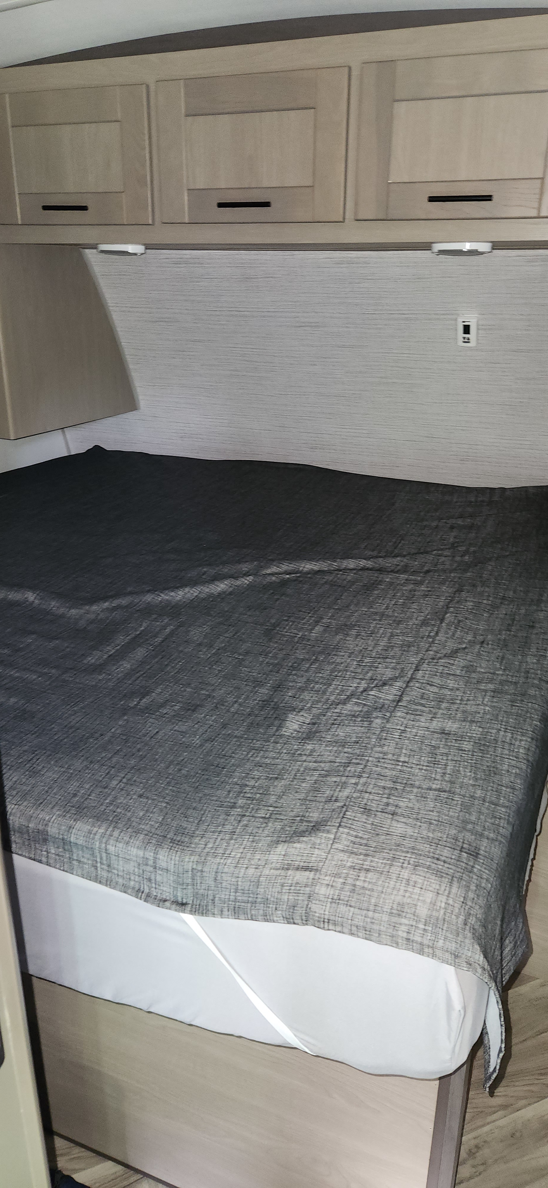 Modern RV rental bedroom featuring a made bed with dark blanket, overhead storage cabinets, and clean interior design.. Cruiser RV Shadow Cruiser 2021