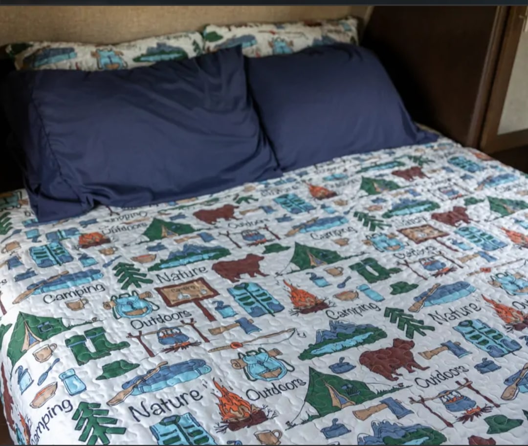 Cozy RV rental bed with camping-themed quilt and navy pillows, featuring tents, bears, and "Nature" text.. Forest River Cherokee Grey Wolf 2016