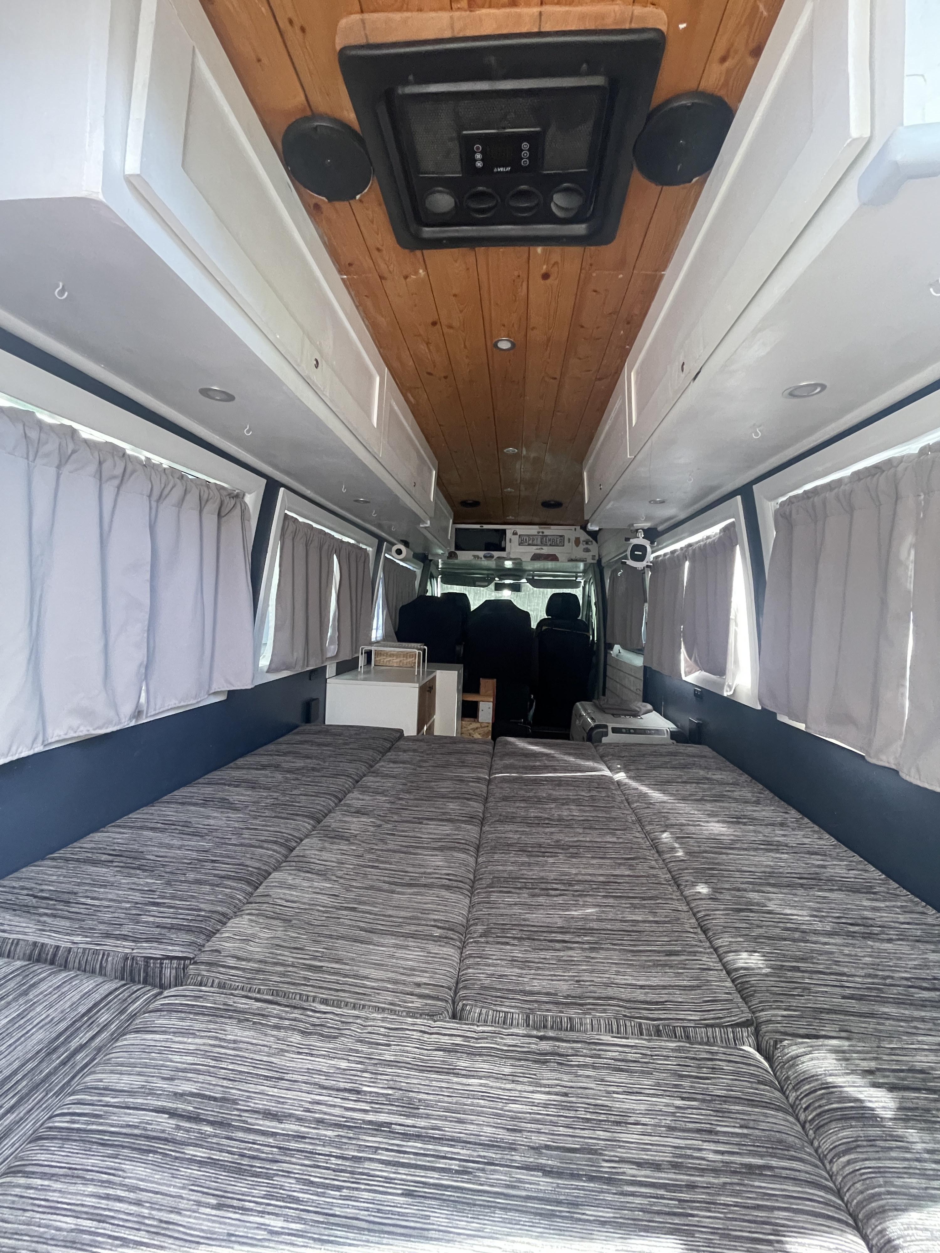 Relax in this RV rental's spacious interior, featuring a striped bed, overhead storage, and window curtains.. Mercedes-Benz Sprinter 2014