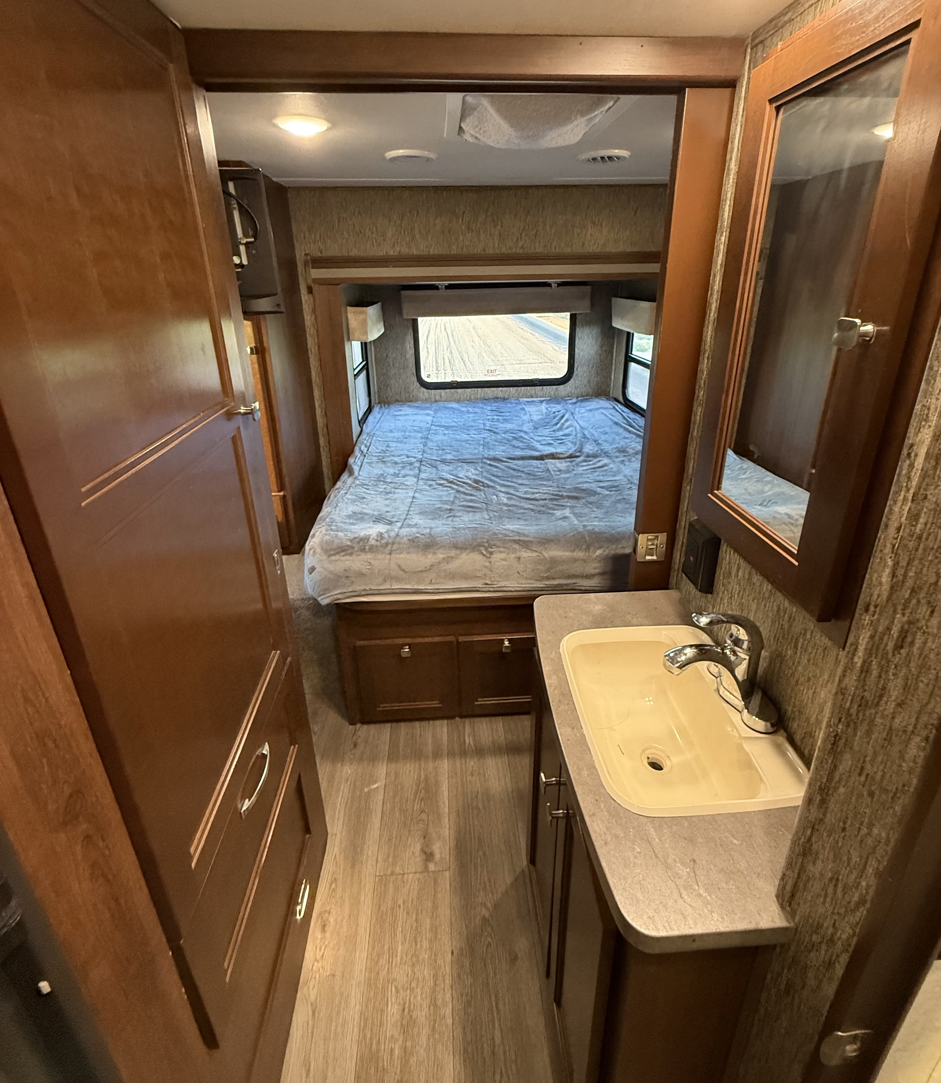 RV rental interior showcasing a comfortable bedroom with windows, a connecting hallway, and a compact bathroom vanity with sink.. Forester MBS 2018
