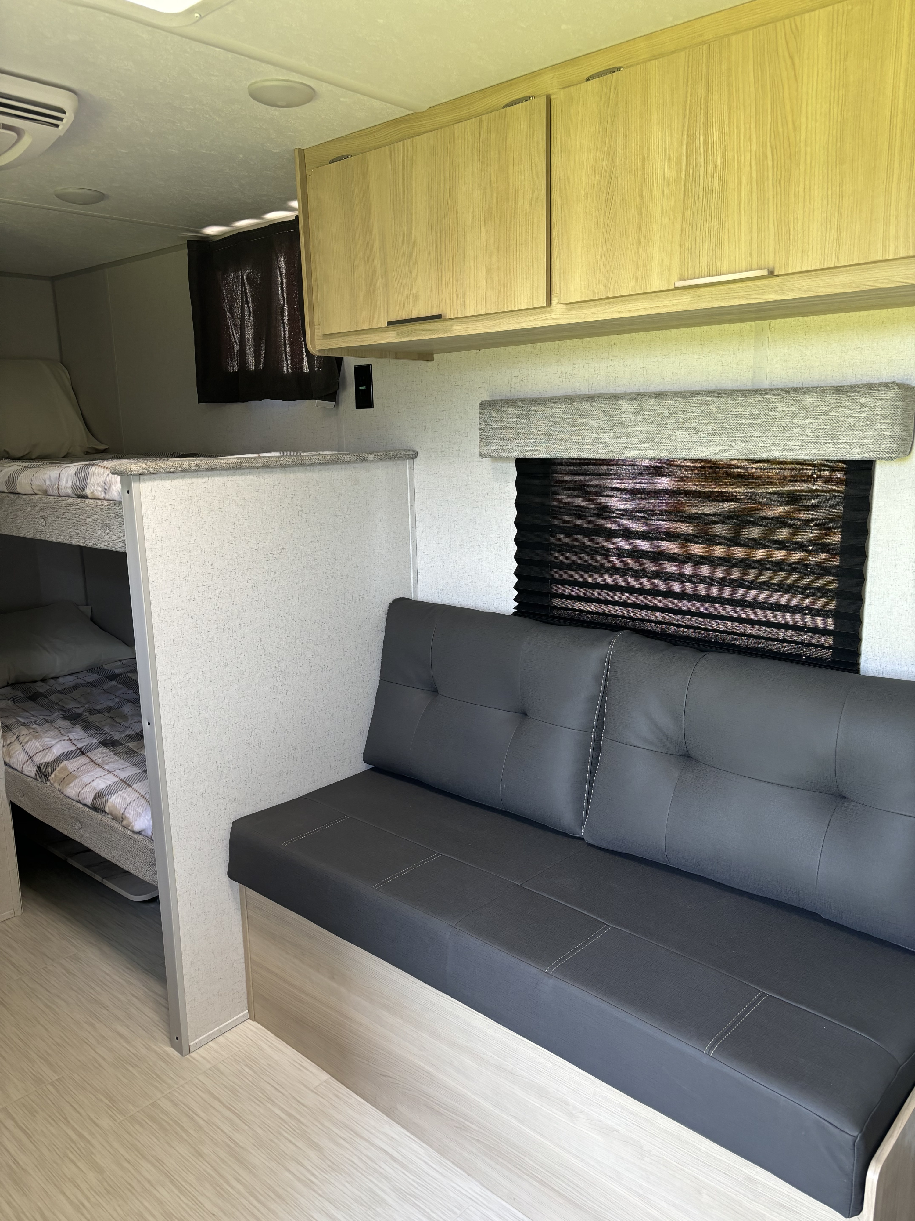 RV rental interior features bunk beds, a dark gray sofa with white stitching, and light wood overhead cabinets.. Forest River Salem FSX 2024