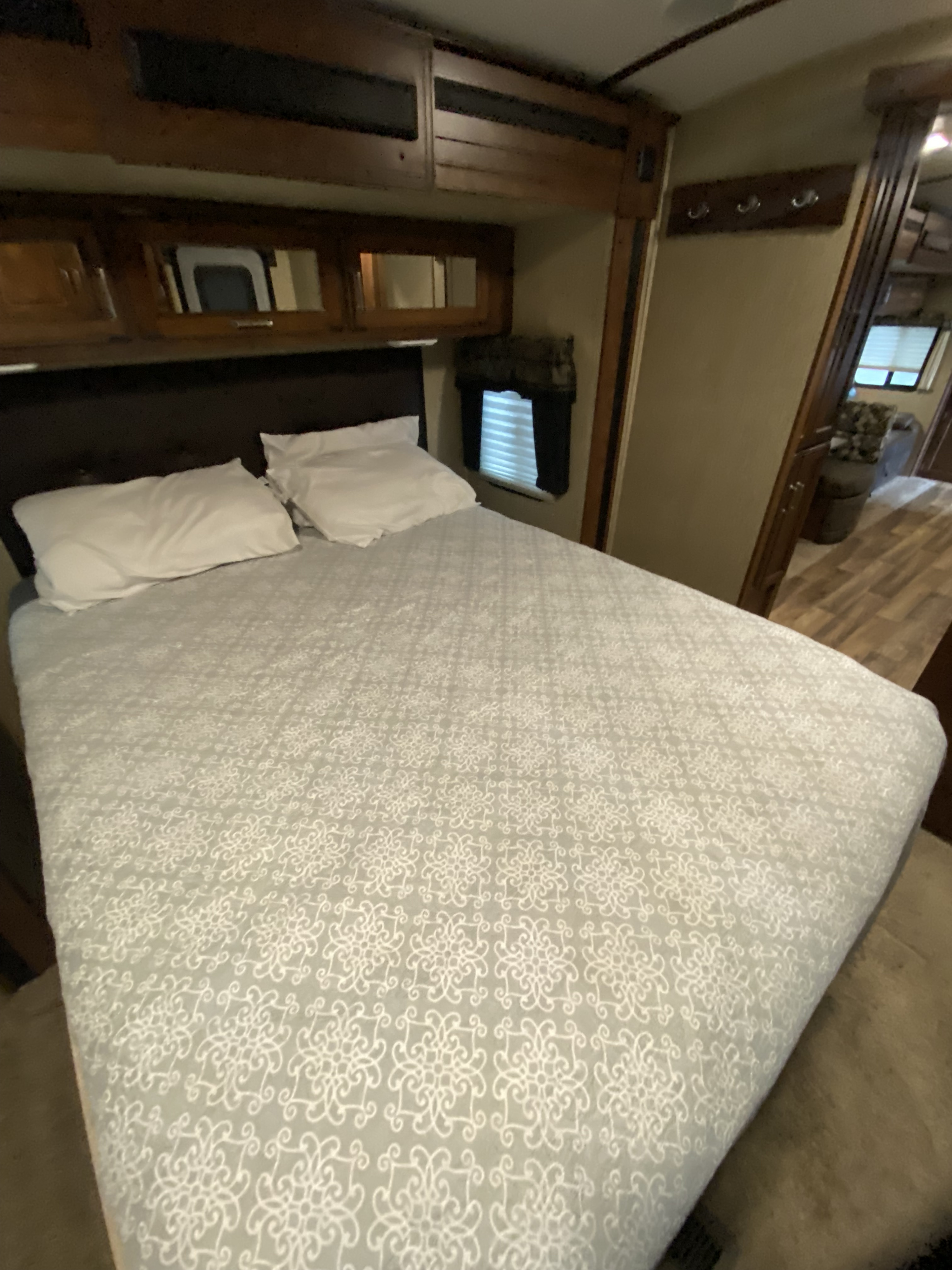 Cozy RV rental bedroom featuring a bed with a white patterned bedspread, pillows, overhead storage, and a window.. Keystone RV Outback Super-Lite Toy Hauler 2017