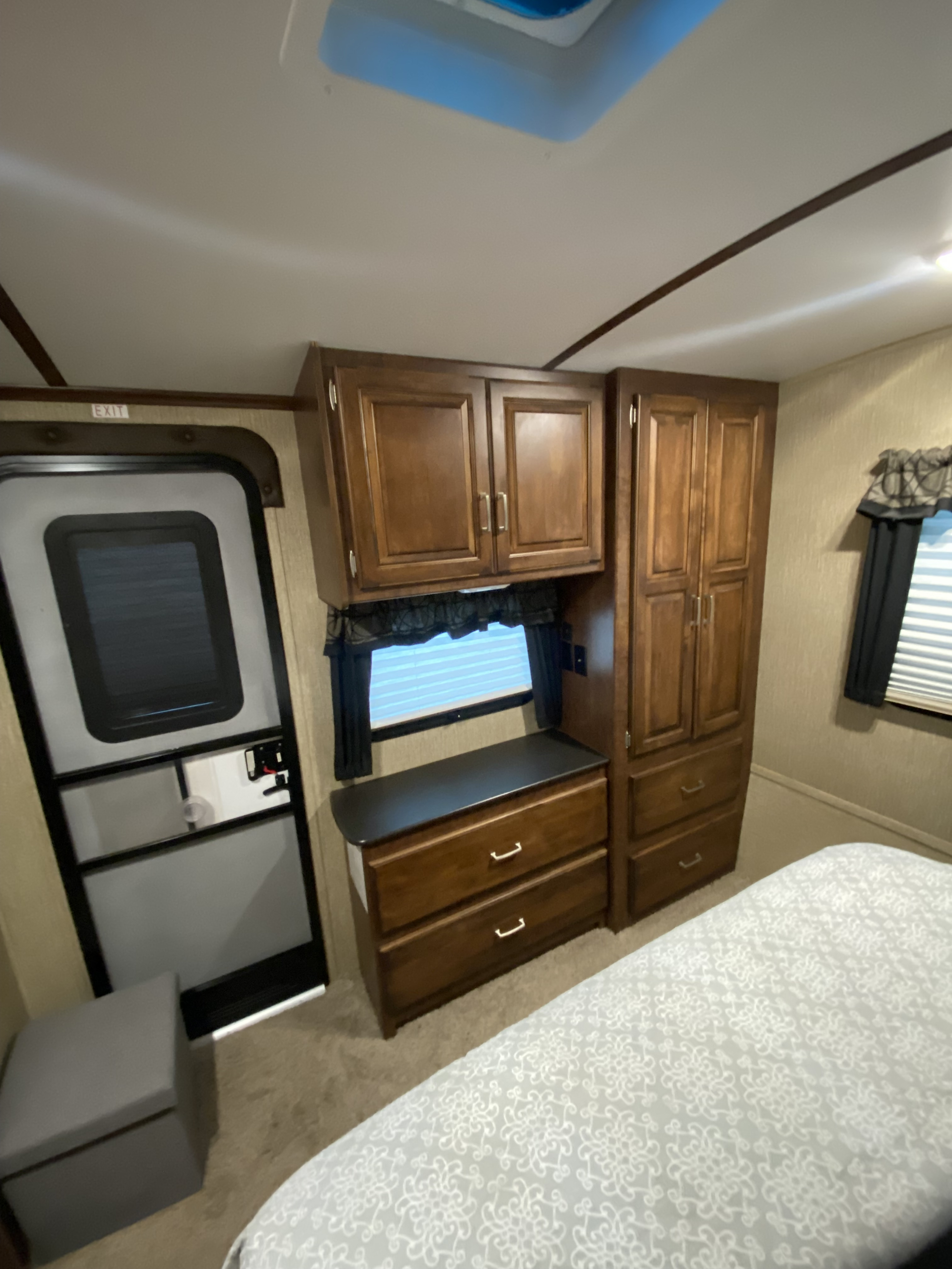 Comfortable RV rental bedroom featuring ample wooden storage, a window, bed, and clear exit for a relaxing trip.. Keystone RV Outback Super-Lite Toy Hauler 2017
