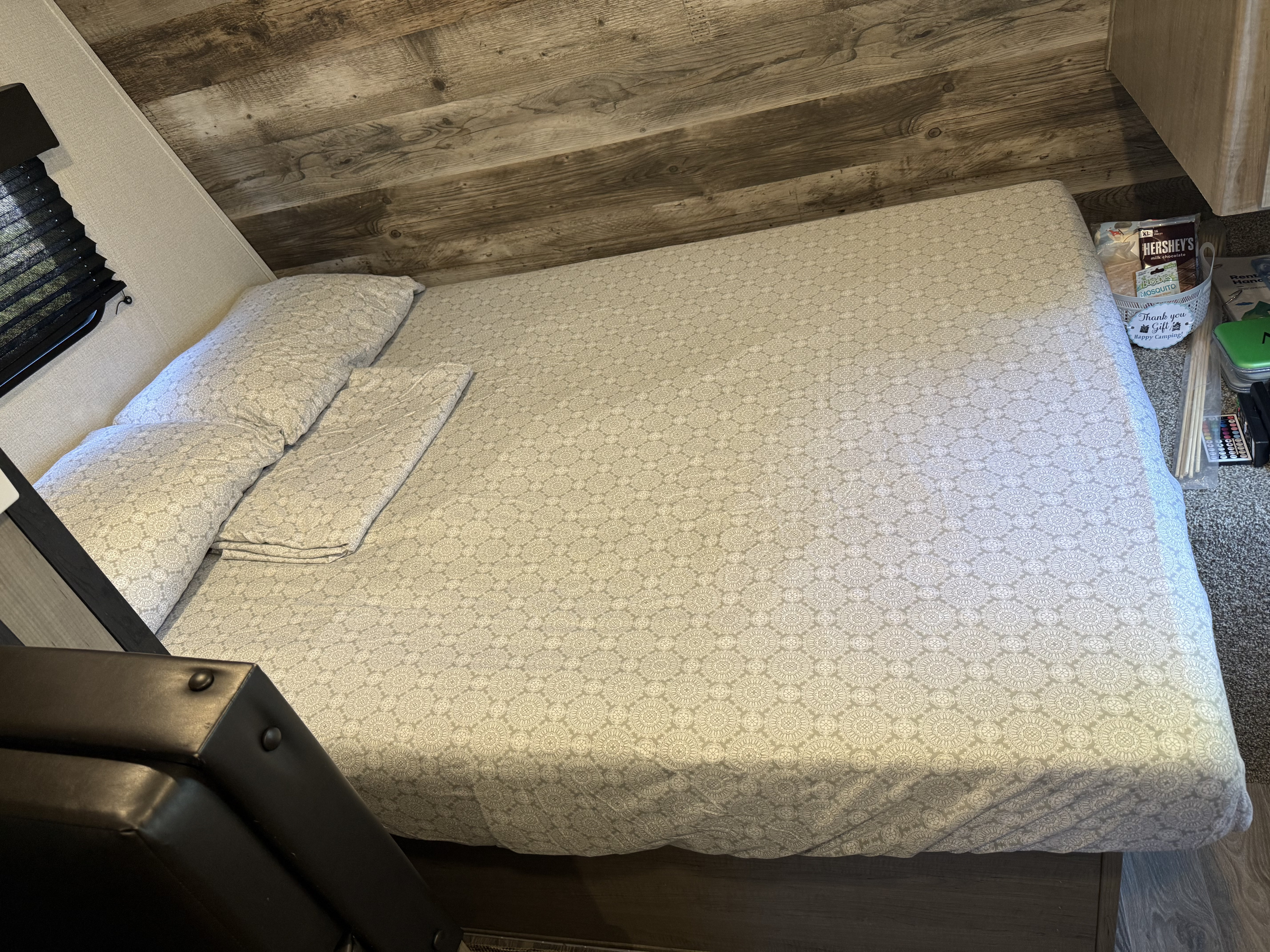 RV rental bed: cozy space with patterned bedding, rustic wood paneling, and a welcome snack basket.. Keystone RV Hideout 2021