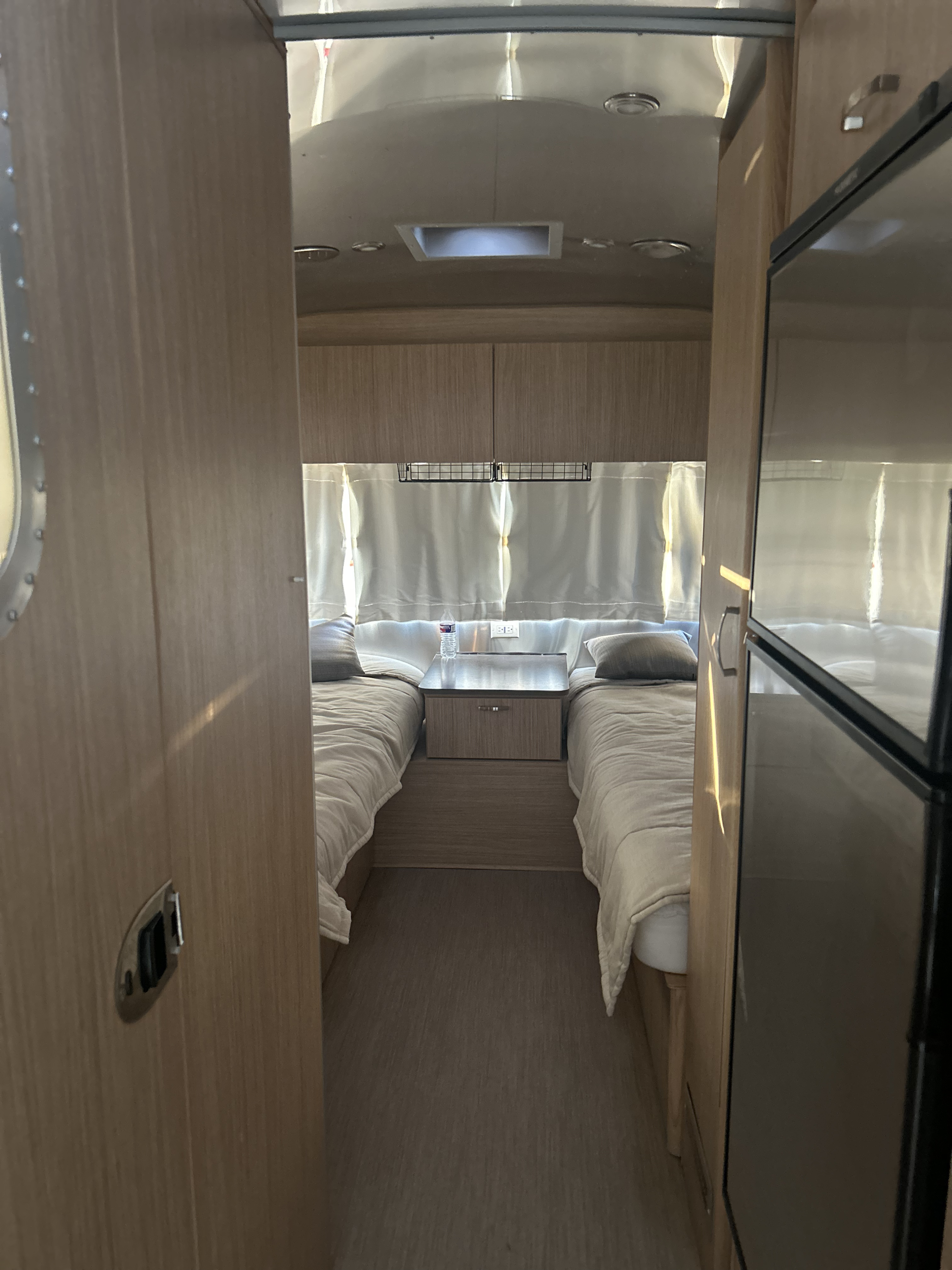 Cozy Airstream RV rental bedroom with twin beds and central nightstand. Features light wood interior and signature metallic ceiling.. Airstream 26RB TWIN 2018