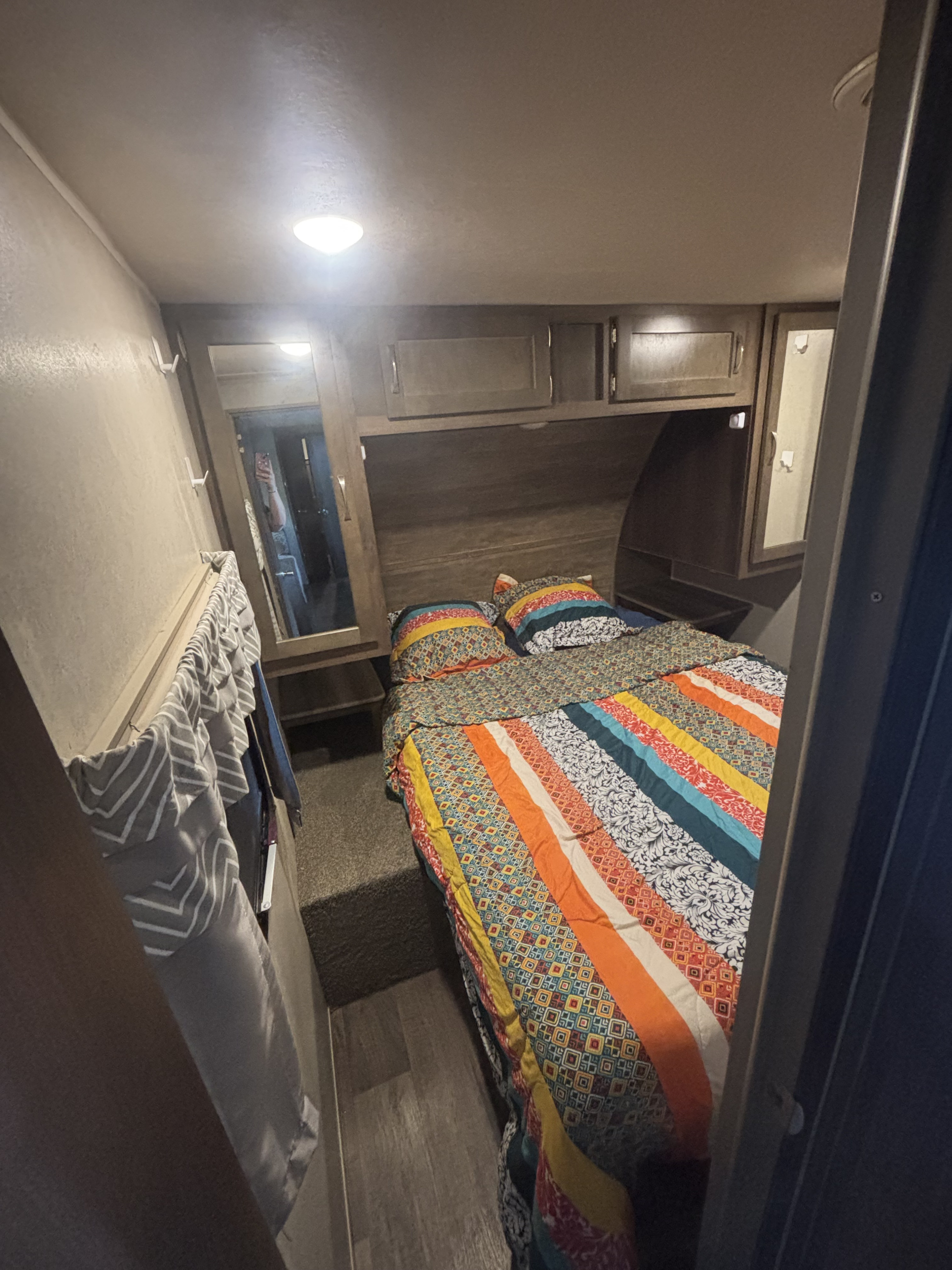 Inside an RV rental bedroom: a cozy bed with vibrant bedding, overhead cabinets, and wall hooks, perfect for compact travel living.. Forest River Palomino Puma 2019