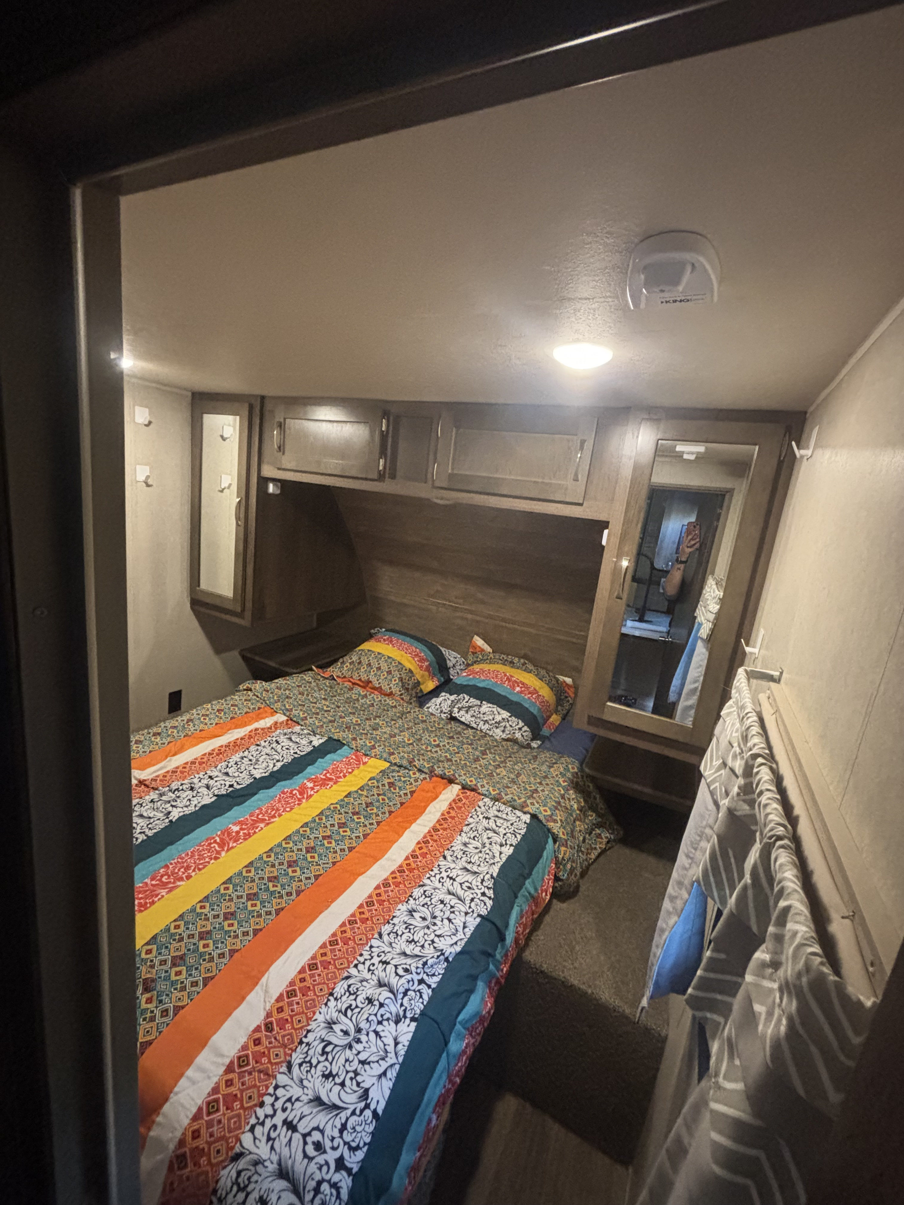 Cozy RV rental bedroom with colorful patterned bedding, overhead cabinets, and wall hooks for essentials.. Forest River Palomino Puma 2019