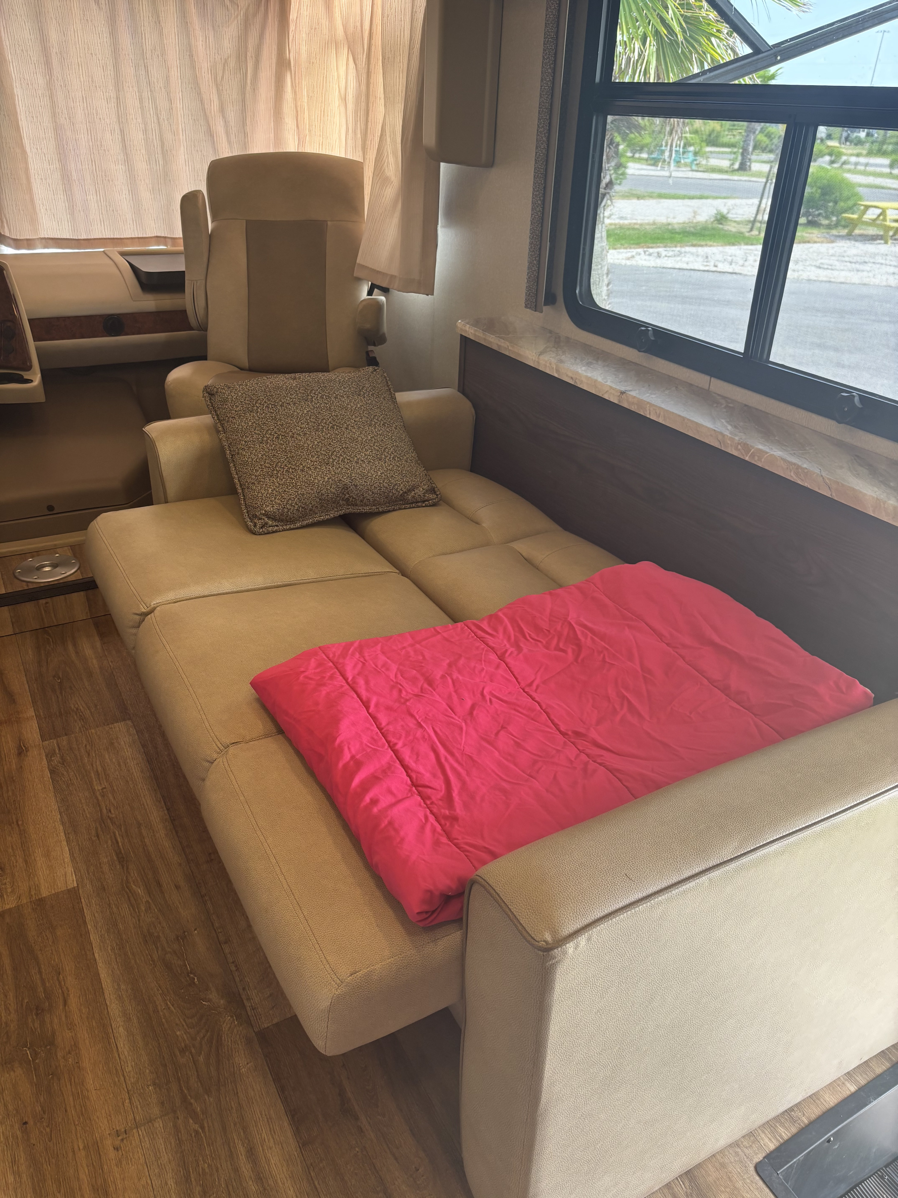 RV rental interior: A tan sofa with a pink blanket, wood flooring, and window views. Ideal for travel.. Coachmen pursuit Precision 27ds 2019