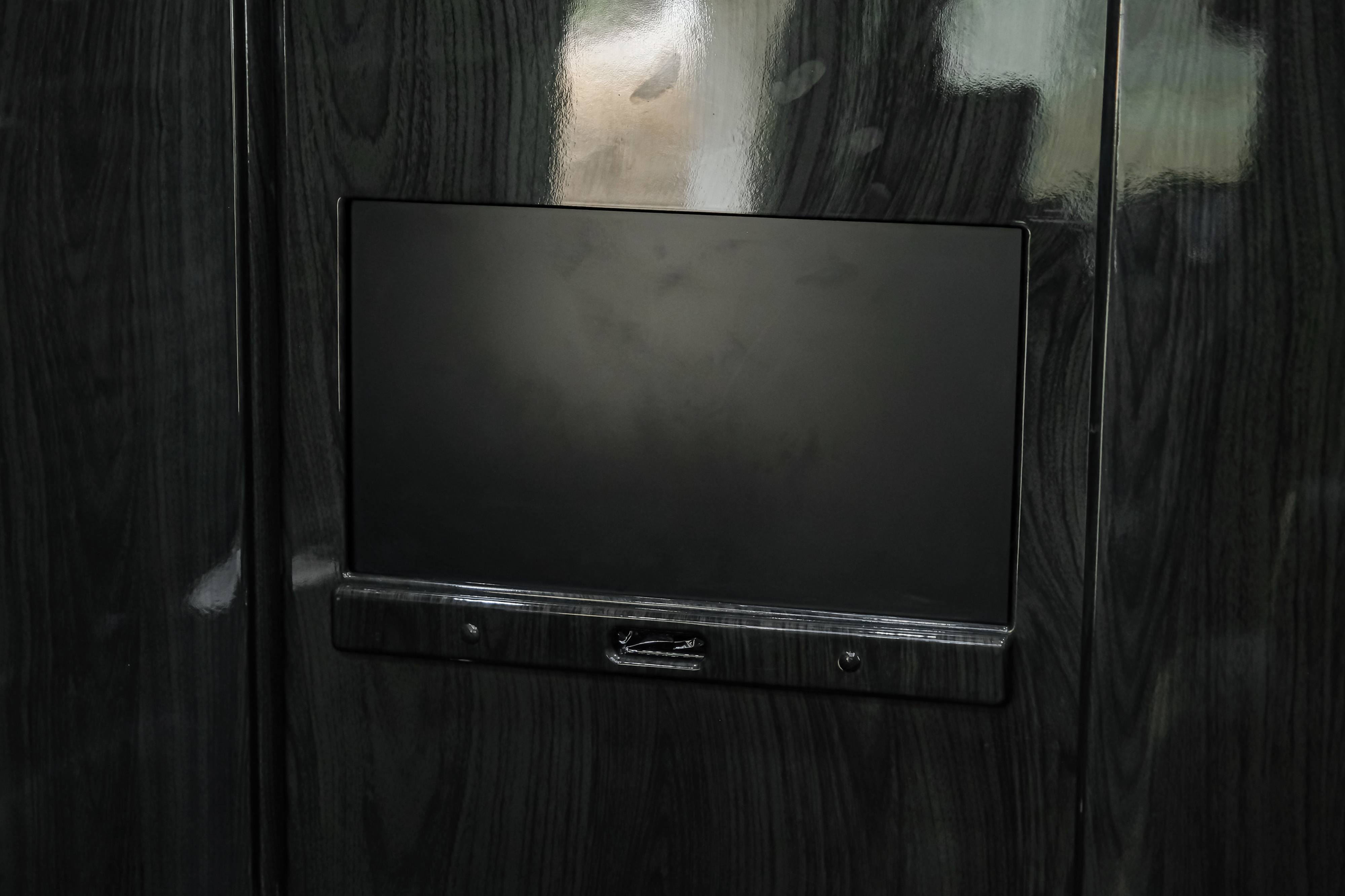RV rental interior: A dark, glossy wood-grained panel features a blank screen and control panel for guests.. Ultimate Toys Ultimate Coach 2021