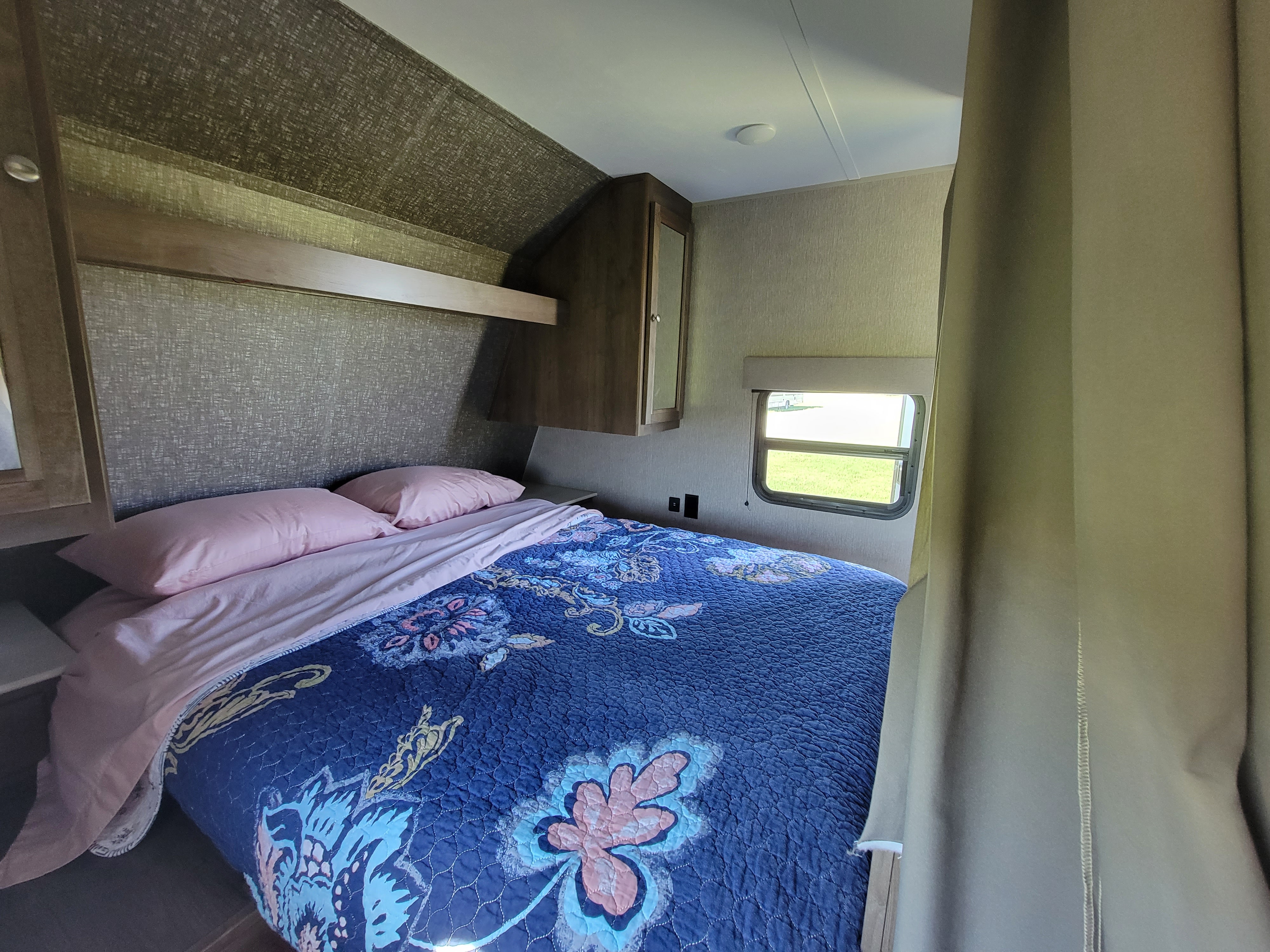 Explore this RV rental's bedroom: comfortable bed with pink pillows, blue quilt, and a window showcasing outdoor views.. Dutchmen Coleman Lantern 2019