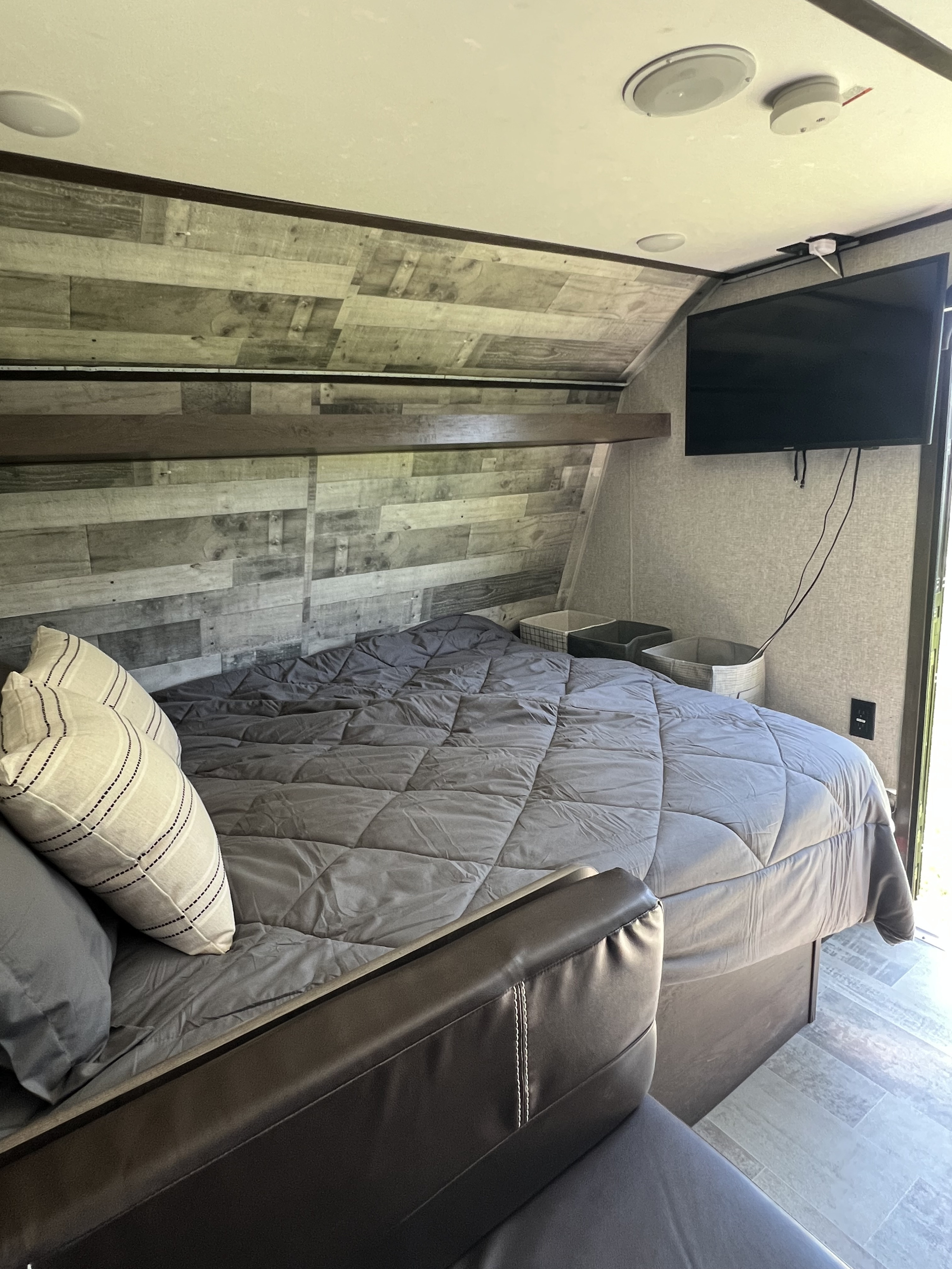 RV rental bedroom: Features a comfy bed with gray comforter, wall-mounted TV, and a stylish wood-planked accent wall.. Dutchmen Coleman Lantern LT 2021